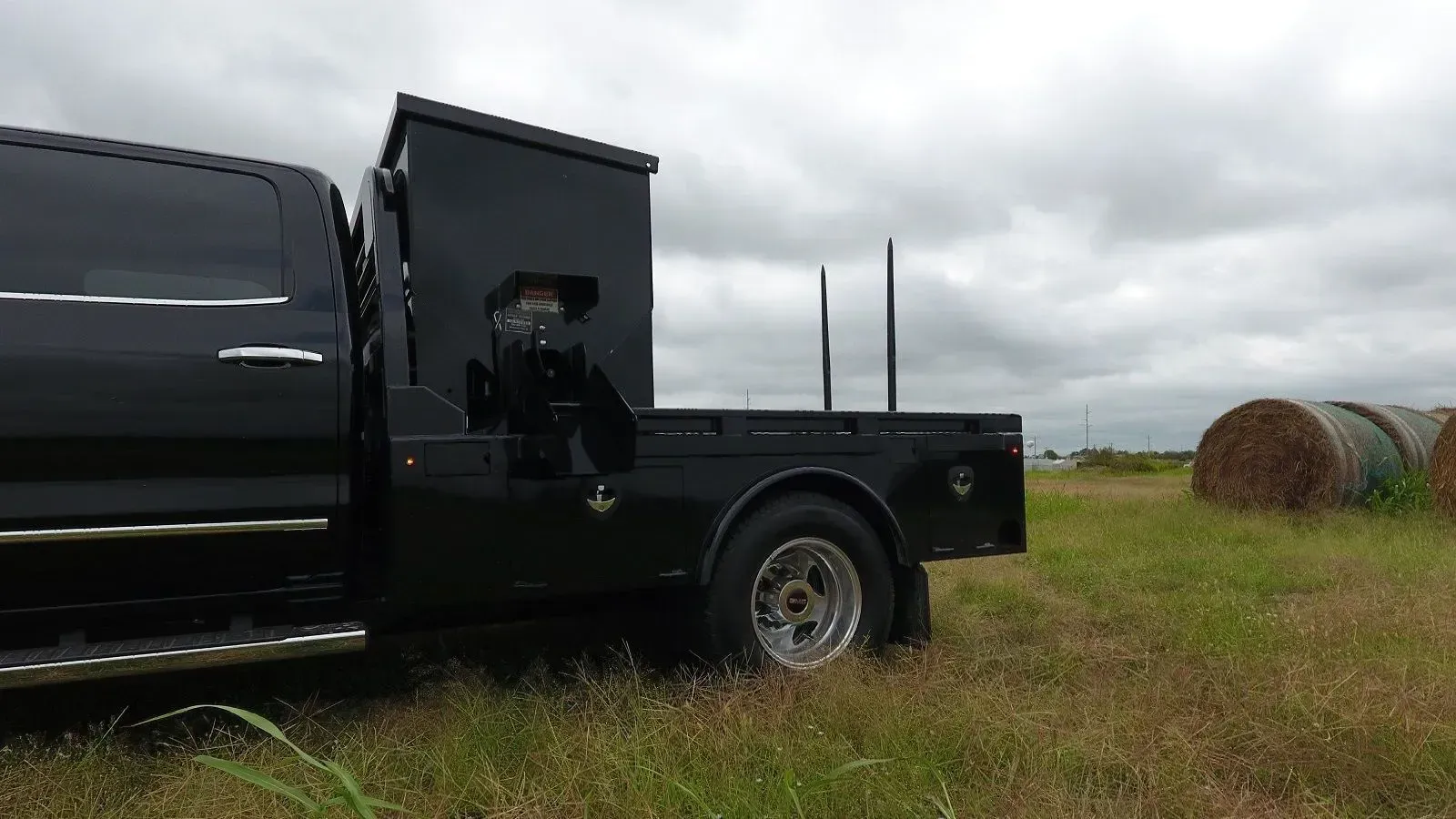 a black ford truck with cube feeder and bale bed is parked in a field with hay bales in the background .