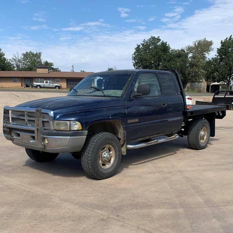 a blue ram truck with a crownline flat bed is parked in a parking lot .