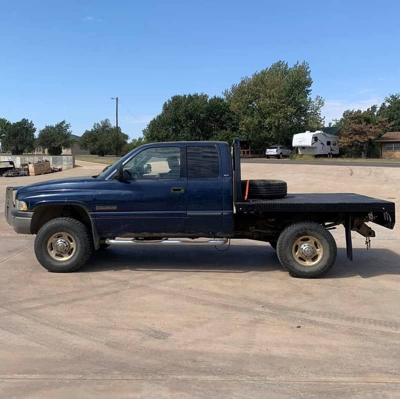 a blue dodge ram truck with a crownline flat bed is parked in a parking lot .