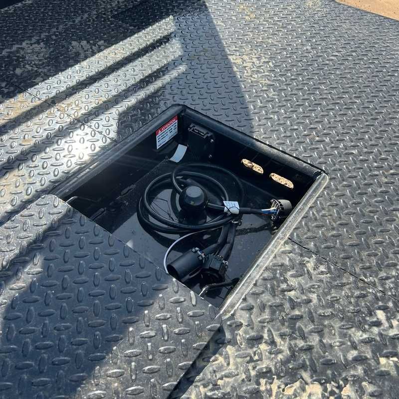 Open gooseneck hatch in diamond-plate deck exposing coiled cable and hardware inside storage compartment