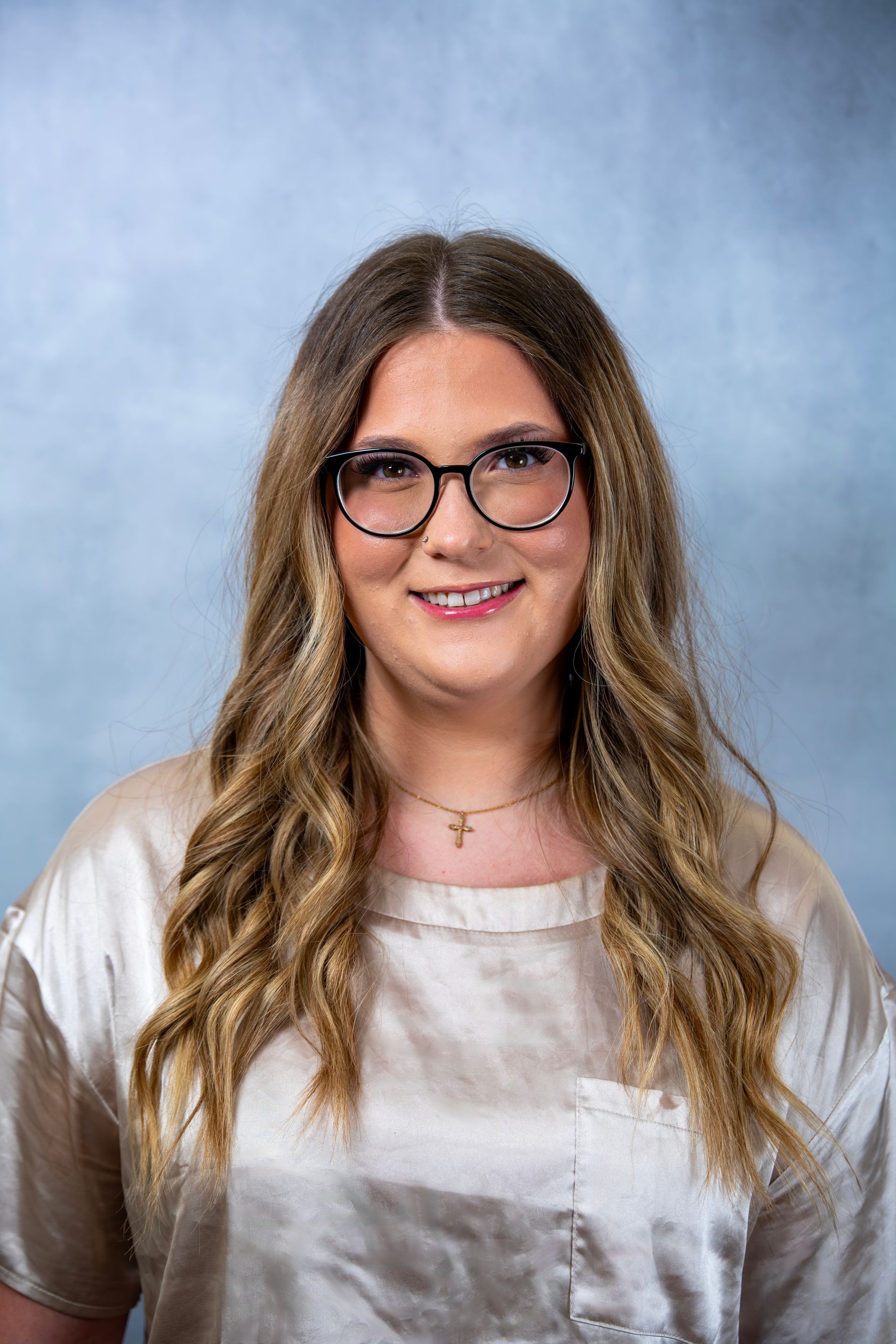 Madi Taylor with long wavy hair, glasses, and a light blouse against a blue studio backdrop