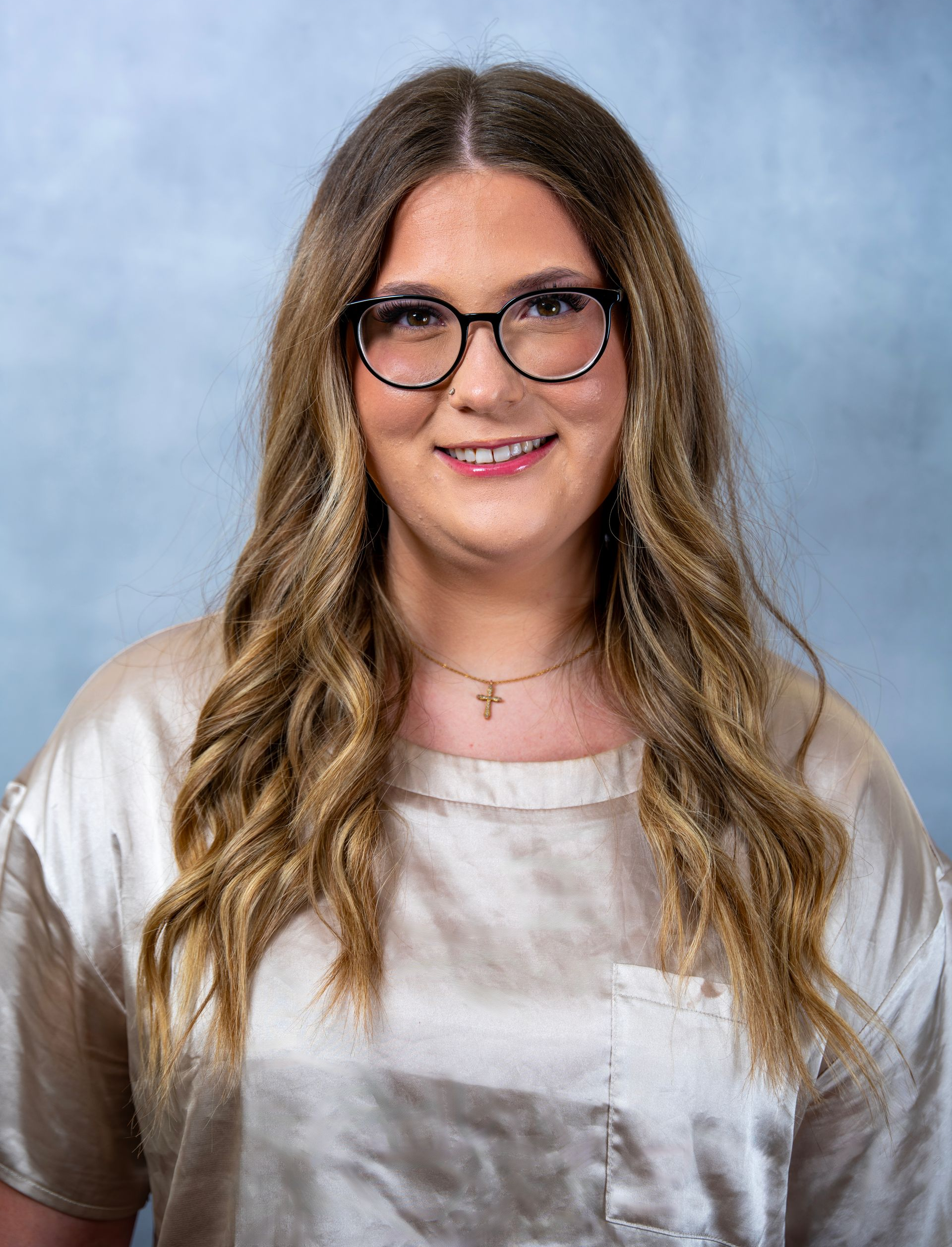 Madi Taylor with glasses, long wavy hair, and a white tie-dye shirt against a blue backdrop