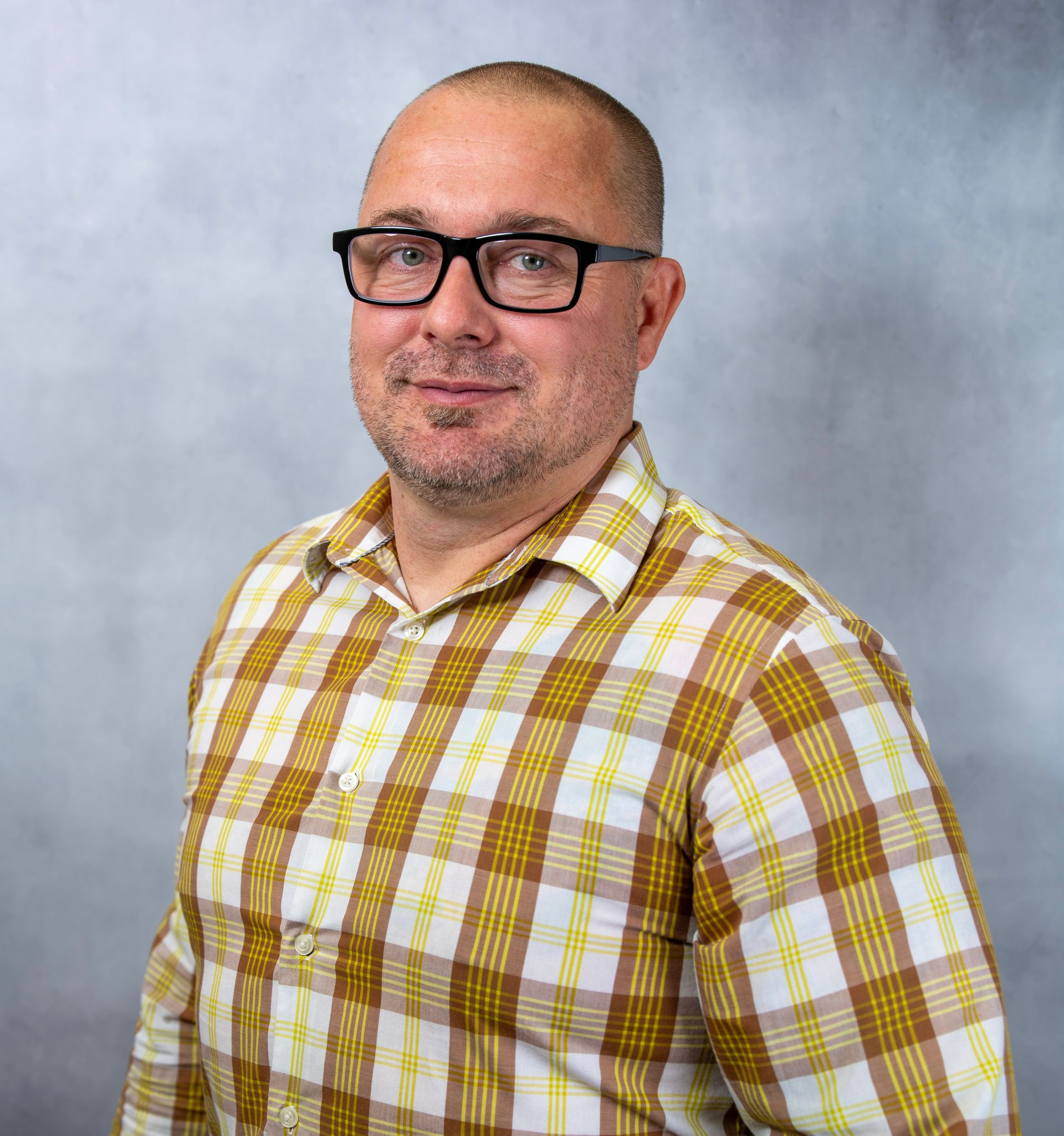 James Fountain wearing glasses and a yellow plaid shirt against a gray backdrop