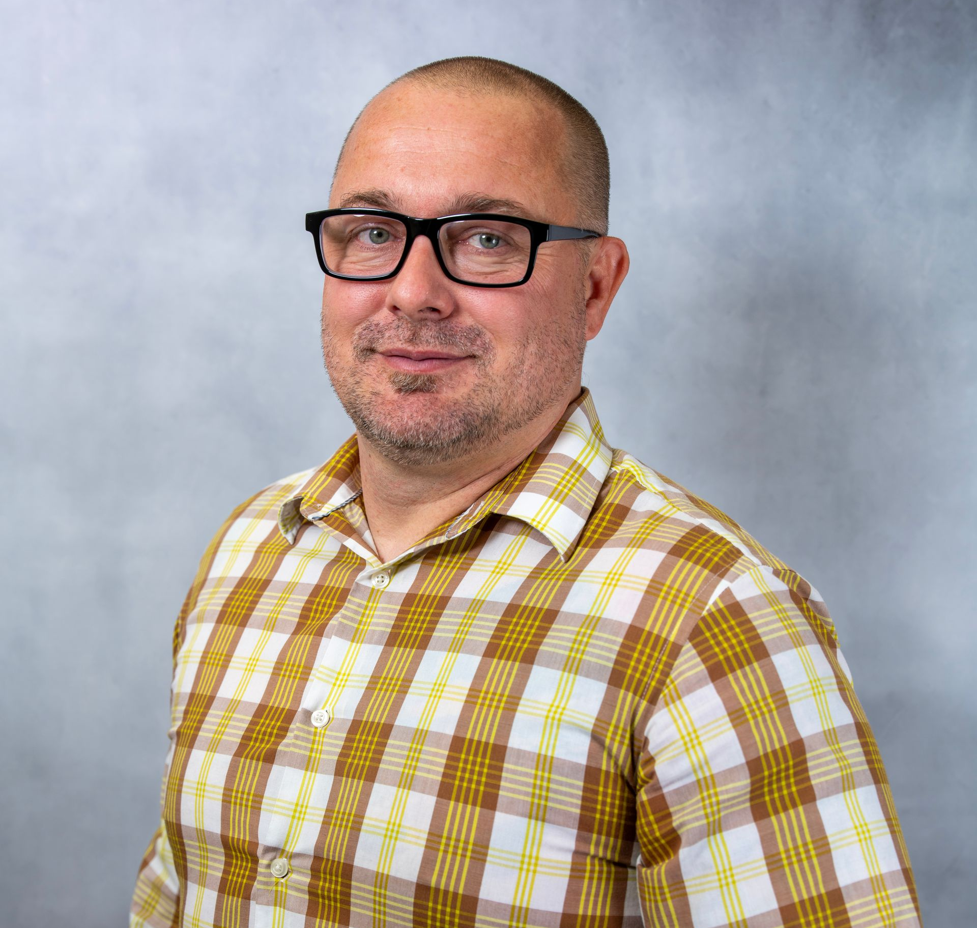 James Fountain wearing black glasses and a yellow plaid shirt against a gray background