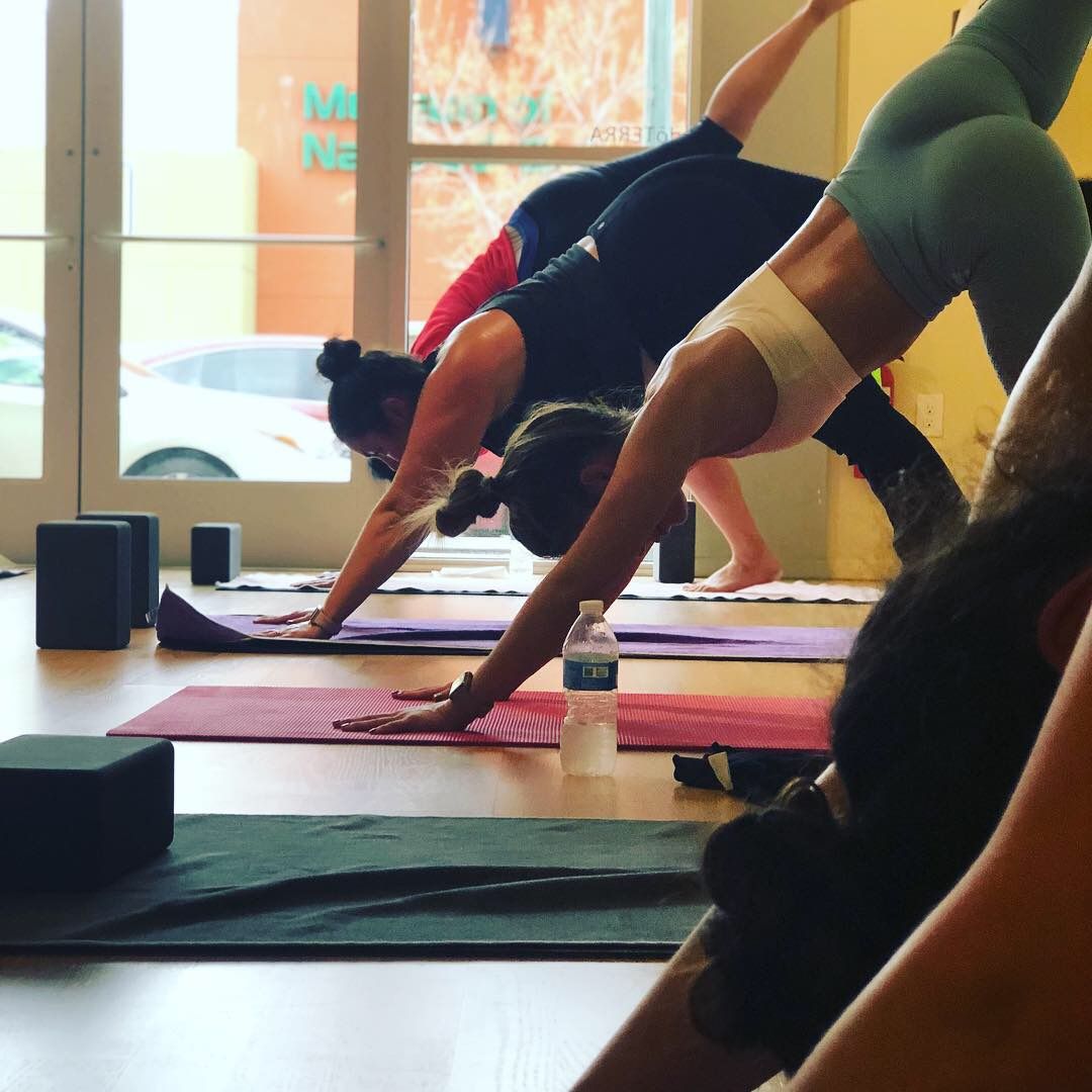 A group of people are doing yoga in front of a window with the word anna on it