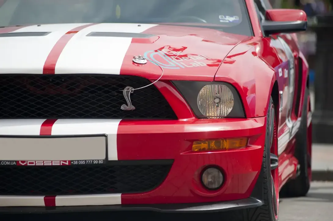 a red mustang with white stripes is parked on the street