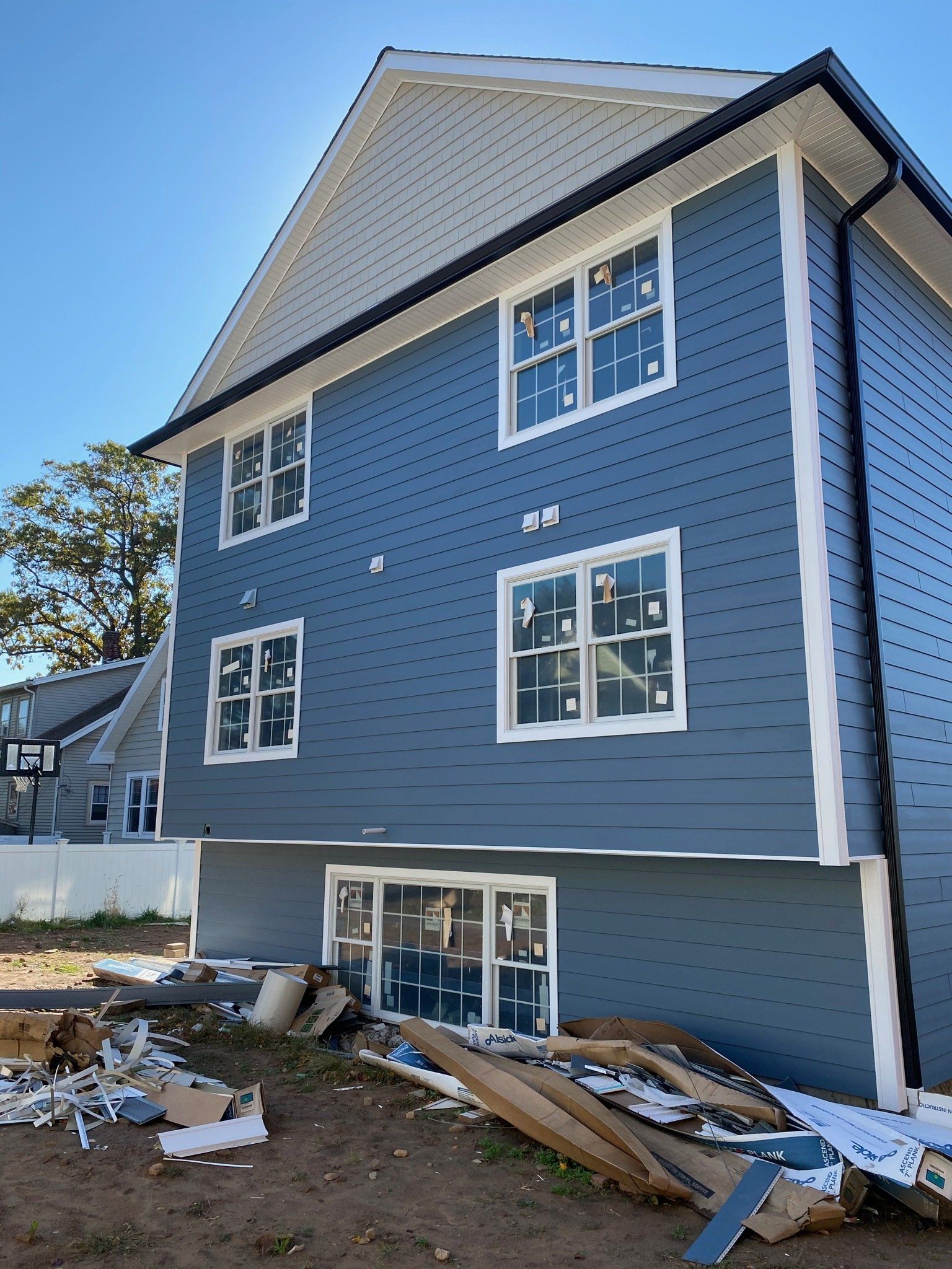 Blue house exterior with white trim, missing lower siding, and construction debris in front