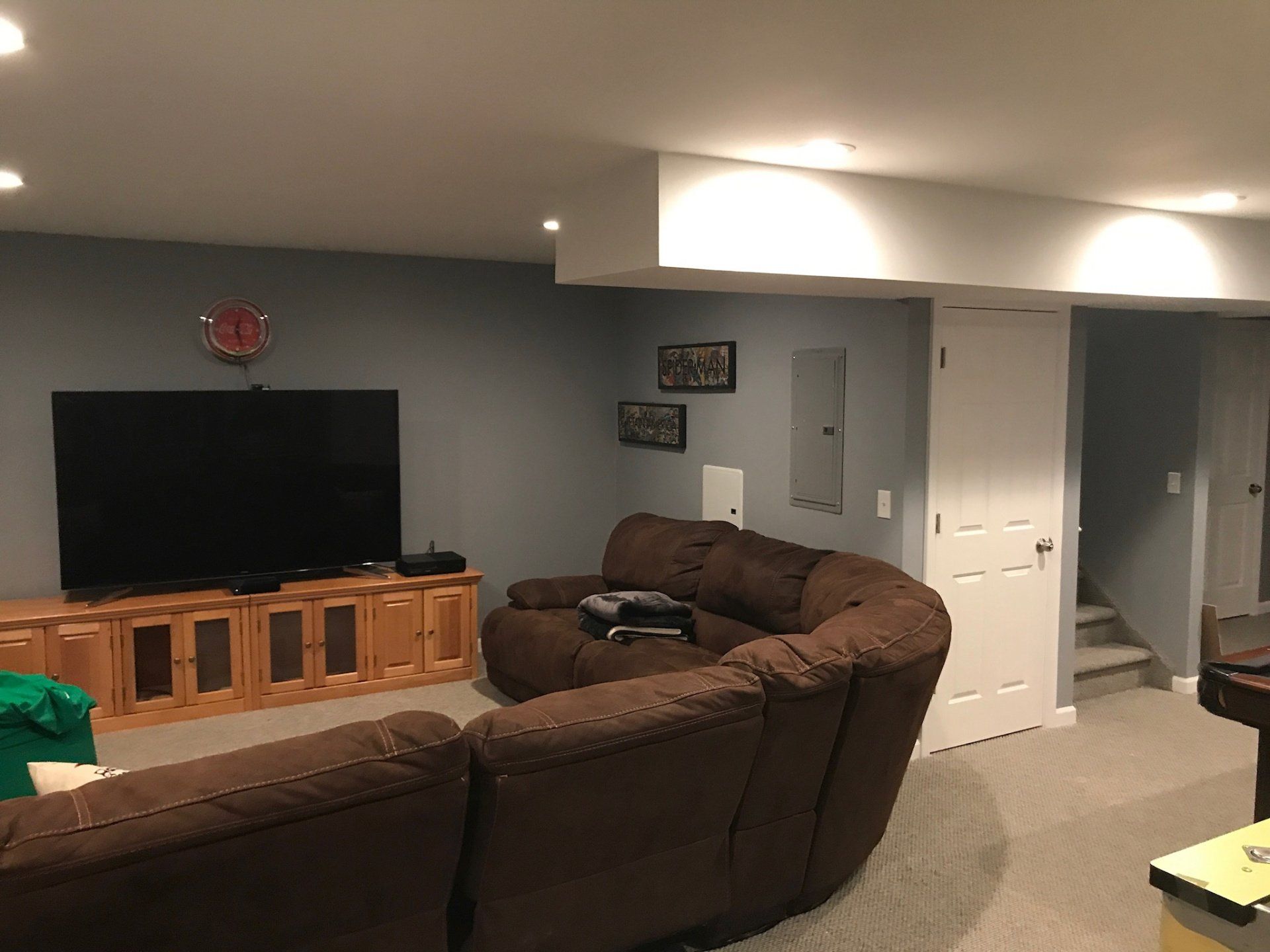 Basement living room with brown sectional, TV on wooden stand, and gray walls