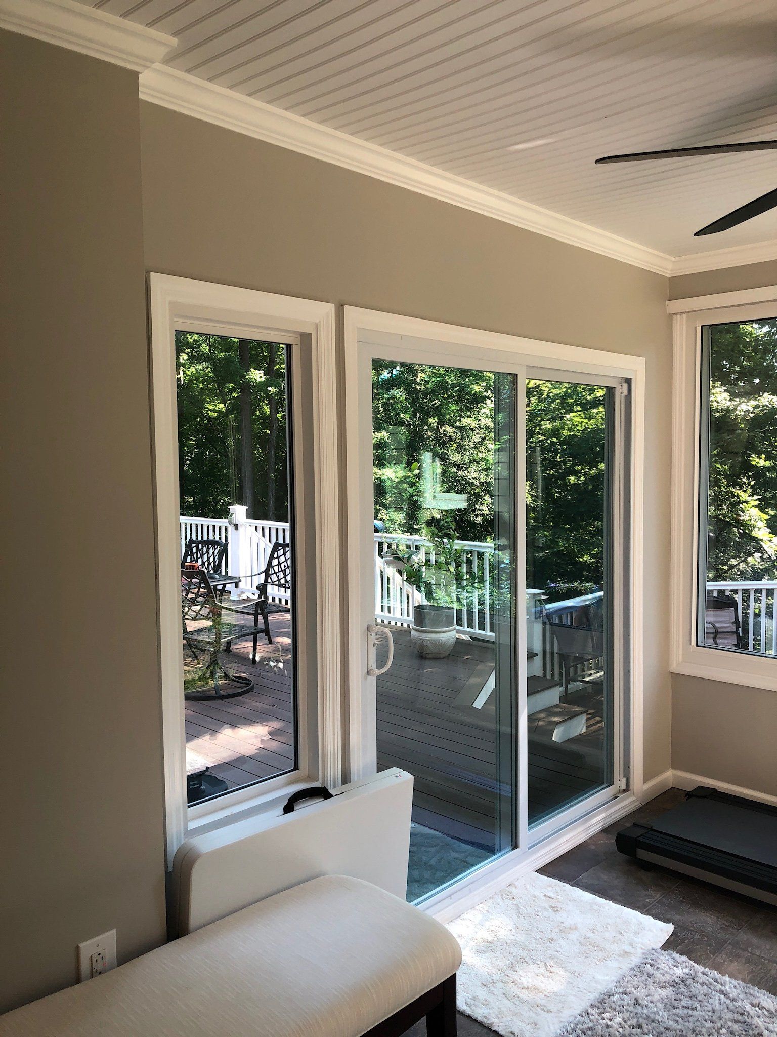 Sunlit living room corner with large glass doors, beige walls, and a white chaise facing a deck.