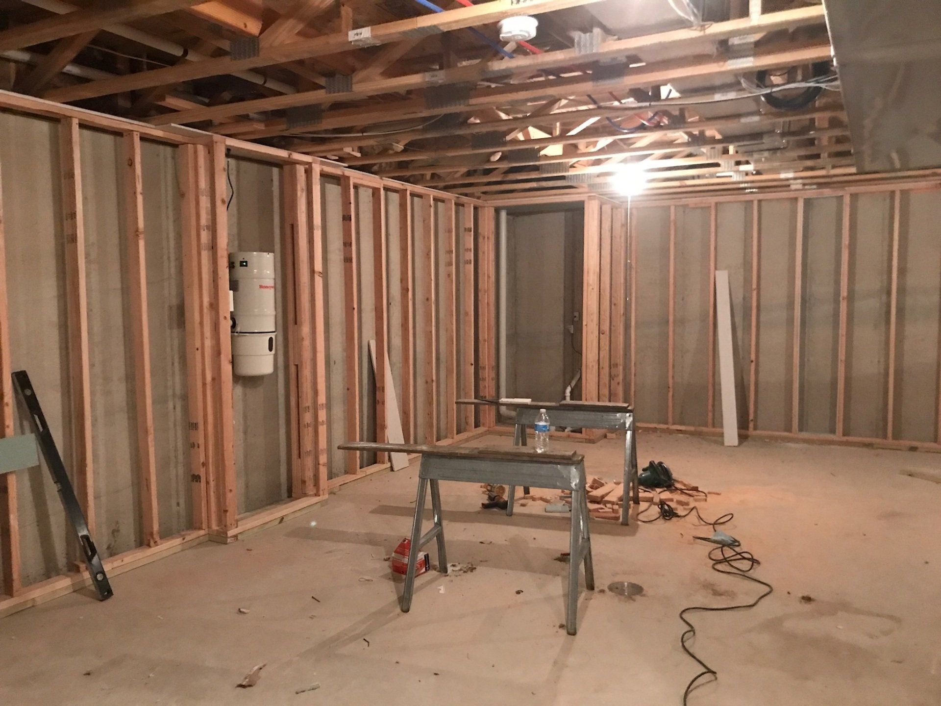 Basement under renovation with exposed studs, tools, and work tables on a concrete floor.