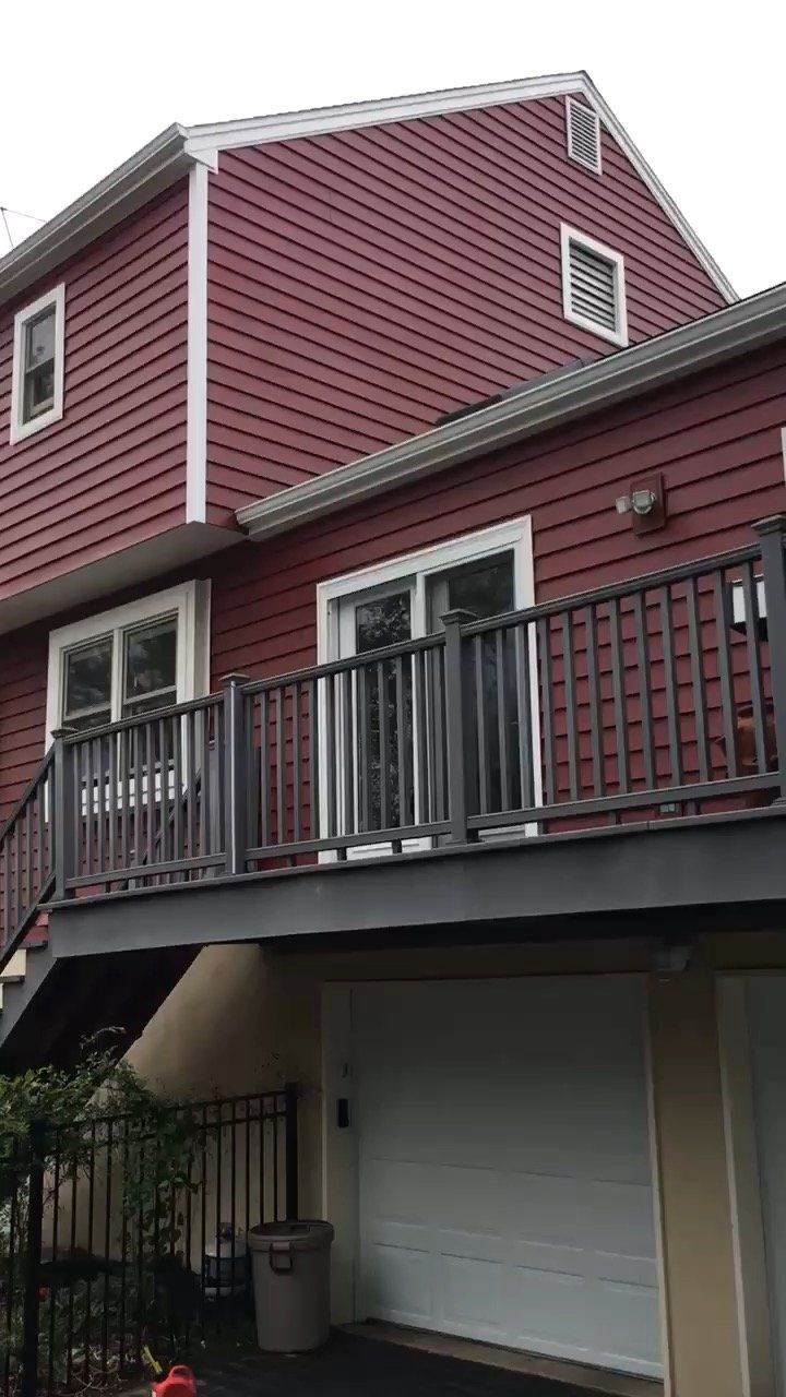 Red house with white trim, balcony railing, and a garage door below