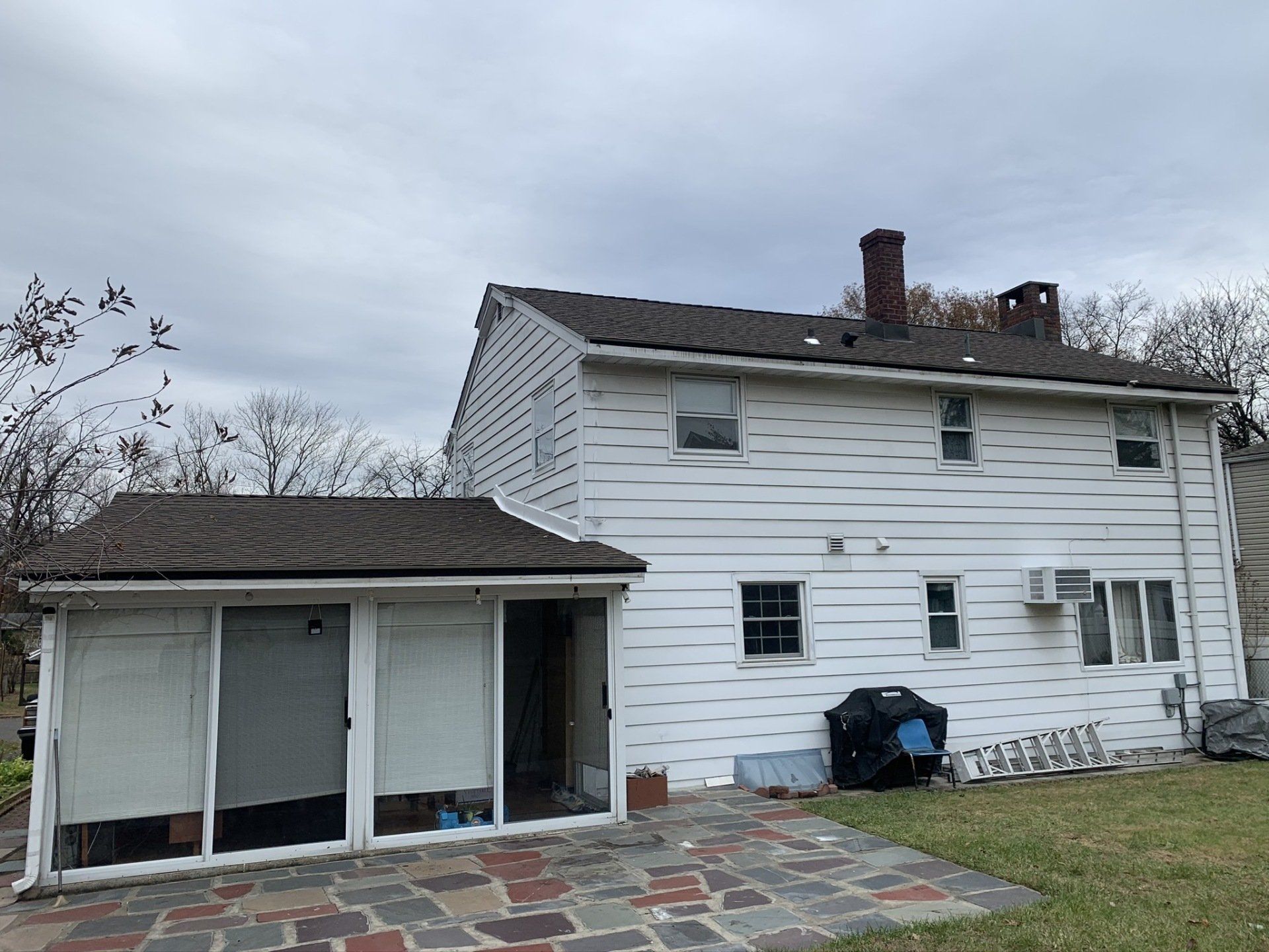 Back of a weathered white house with a small screened porch and yard under an overcast sky