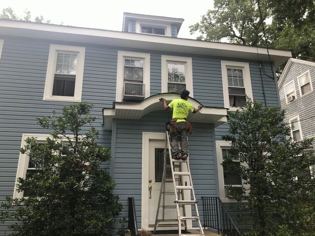 Worker on ladder repairing the awning above a blue house entrance