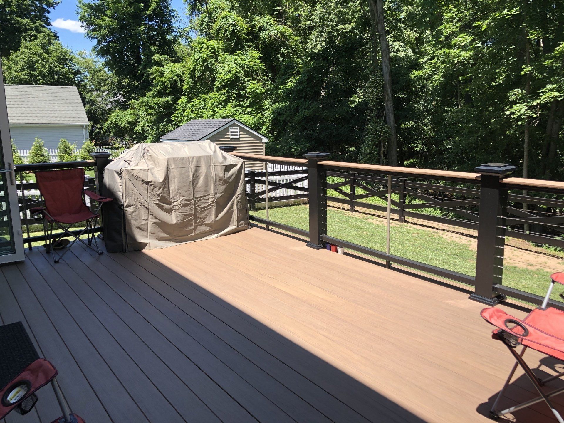 Wooden deck with a covered grill, railing, and red chair beside a green backyard.