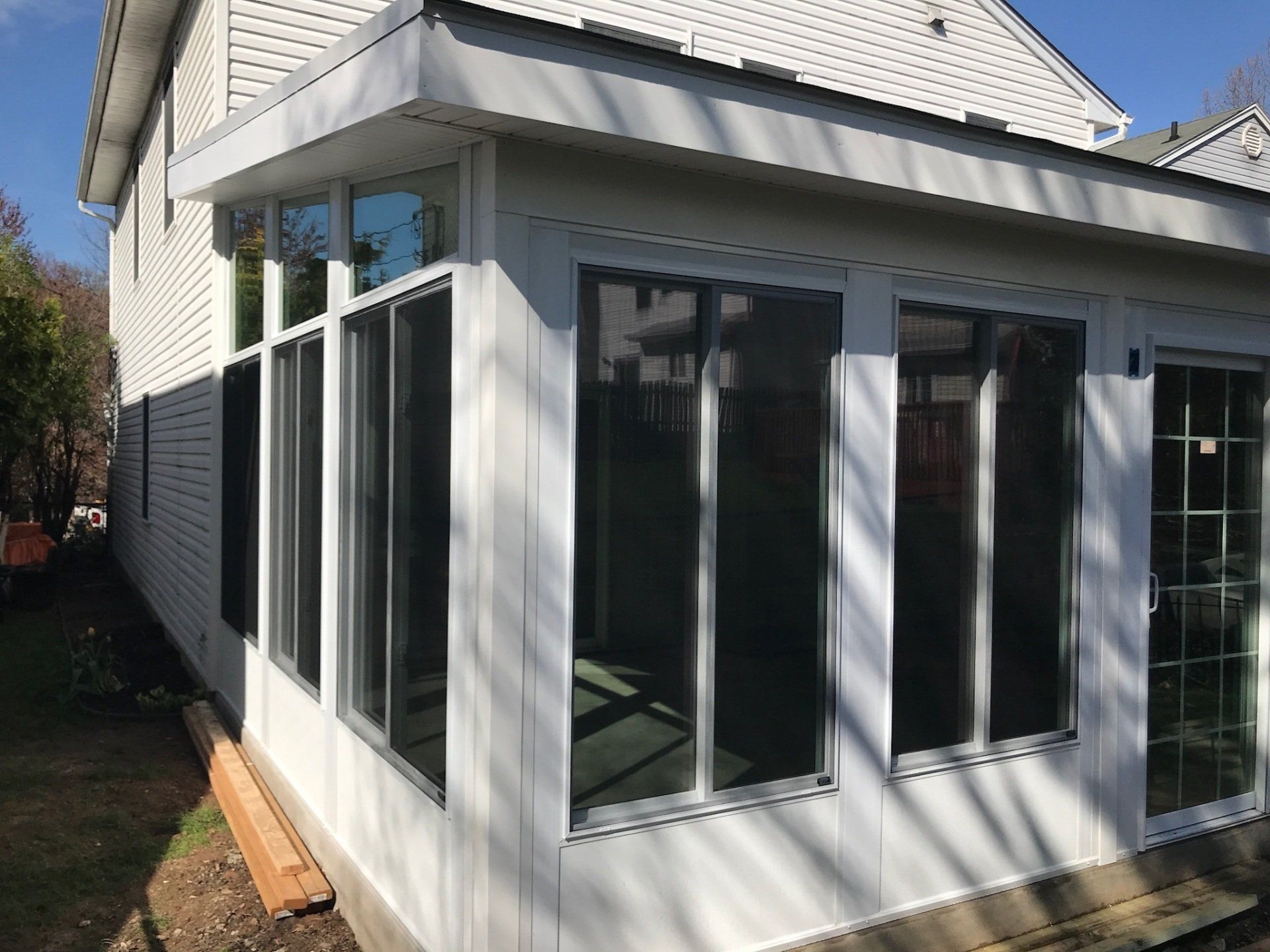 White sunroom addition with large windows on a house exterior, shown from the side in daylight