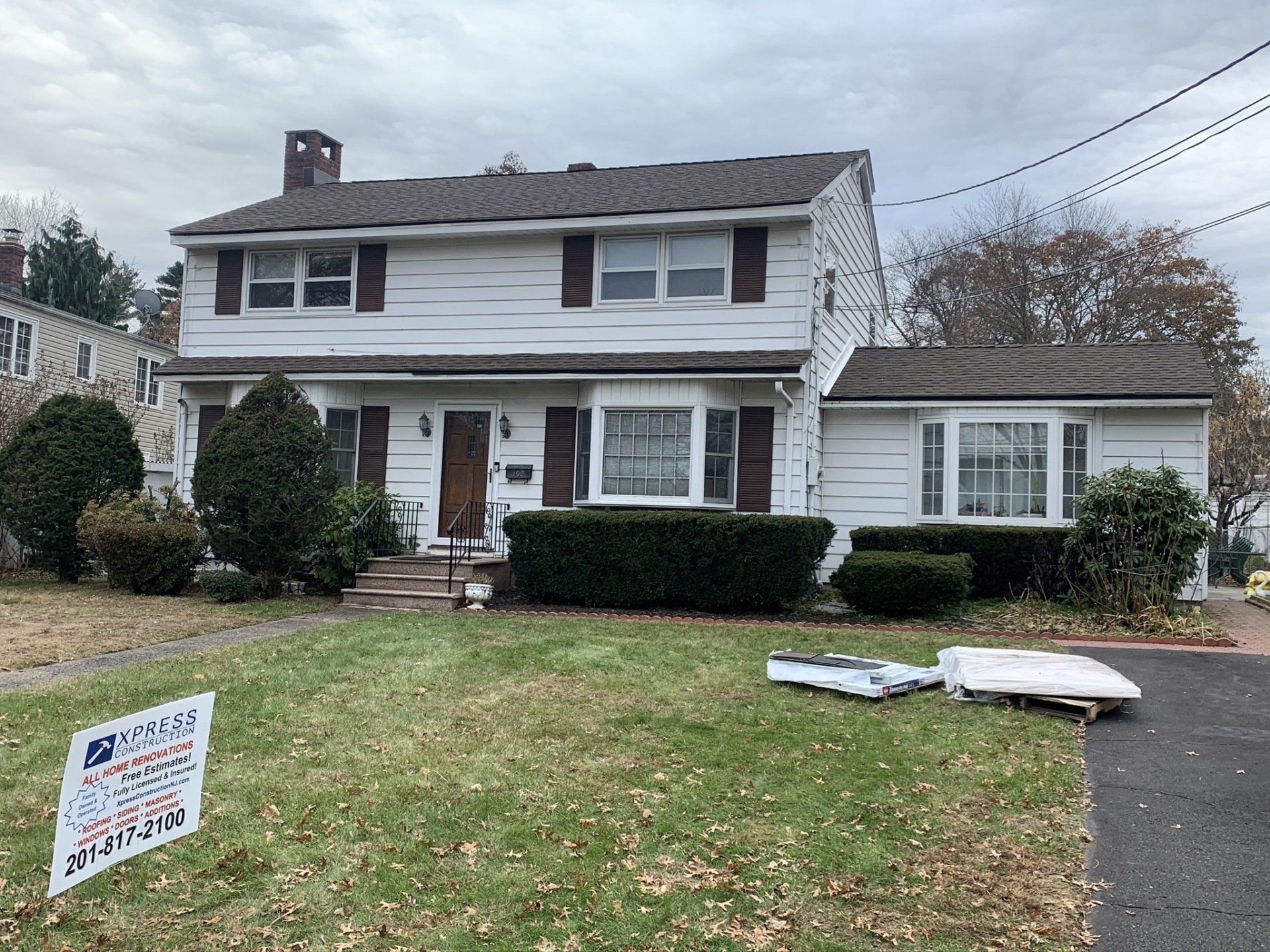 Two-story white house with a lawn and a real estate sign in front under cloudy skies
