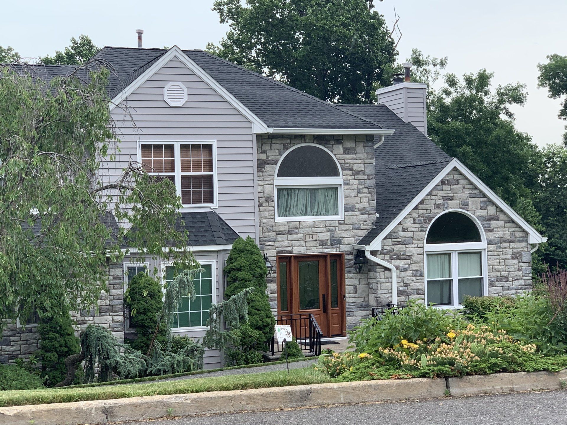 Stone house with gray siding, arched windows, and a landscaped front garden.