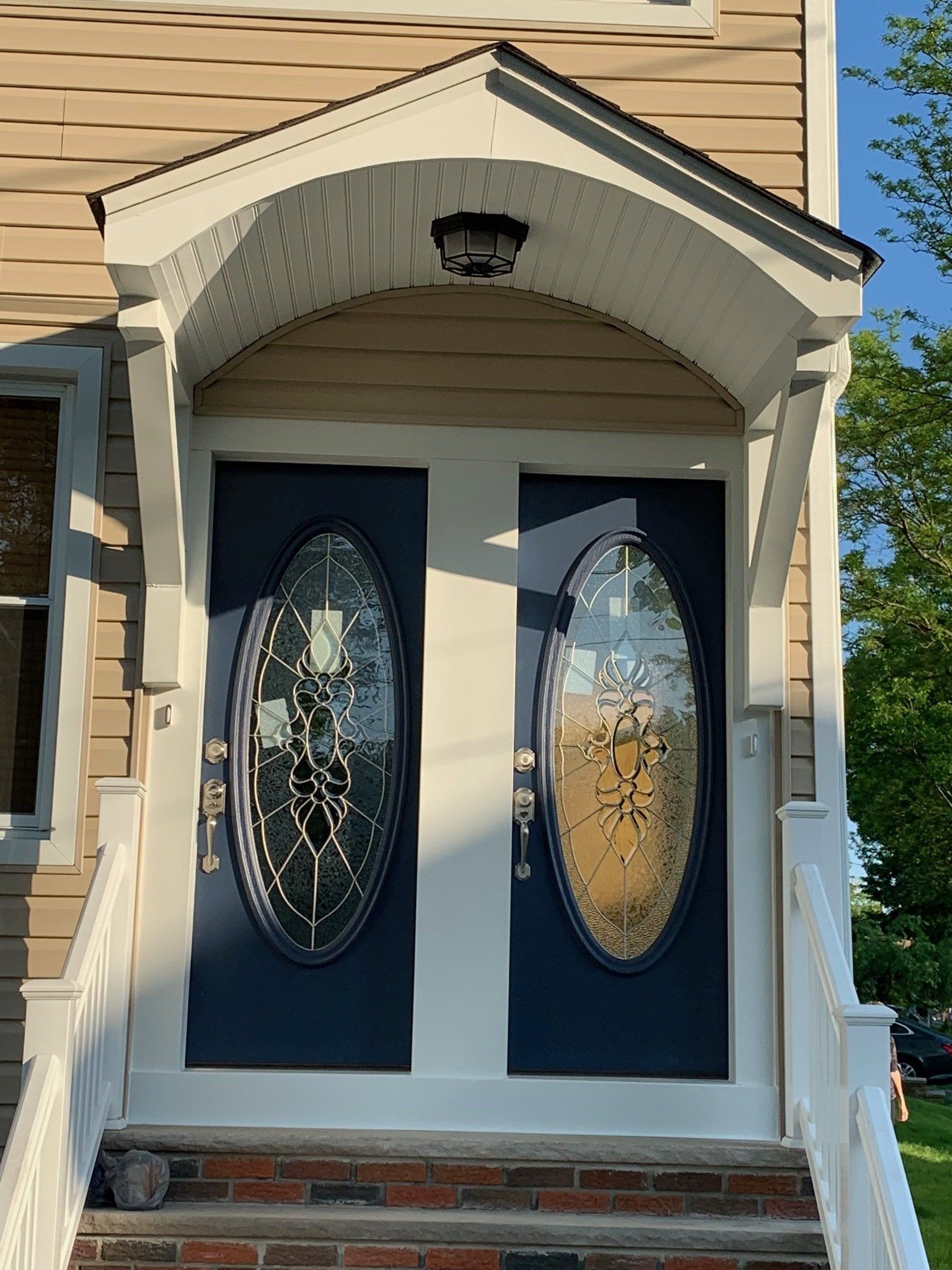 Front porch with two dark blue decorative glass doors and white trim under a beige gable roof.