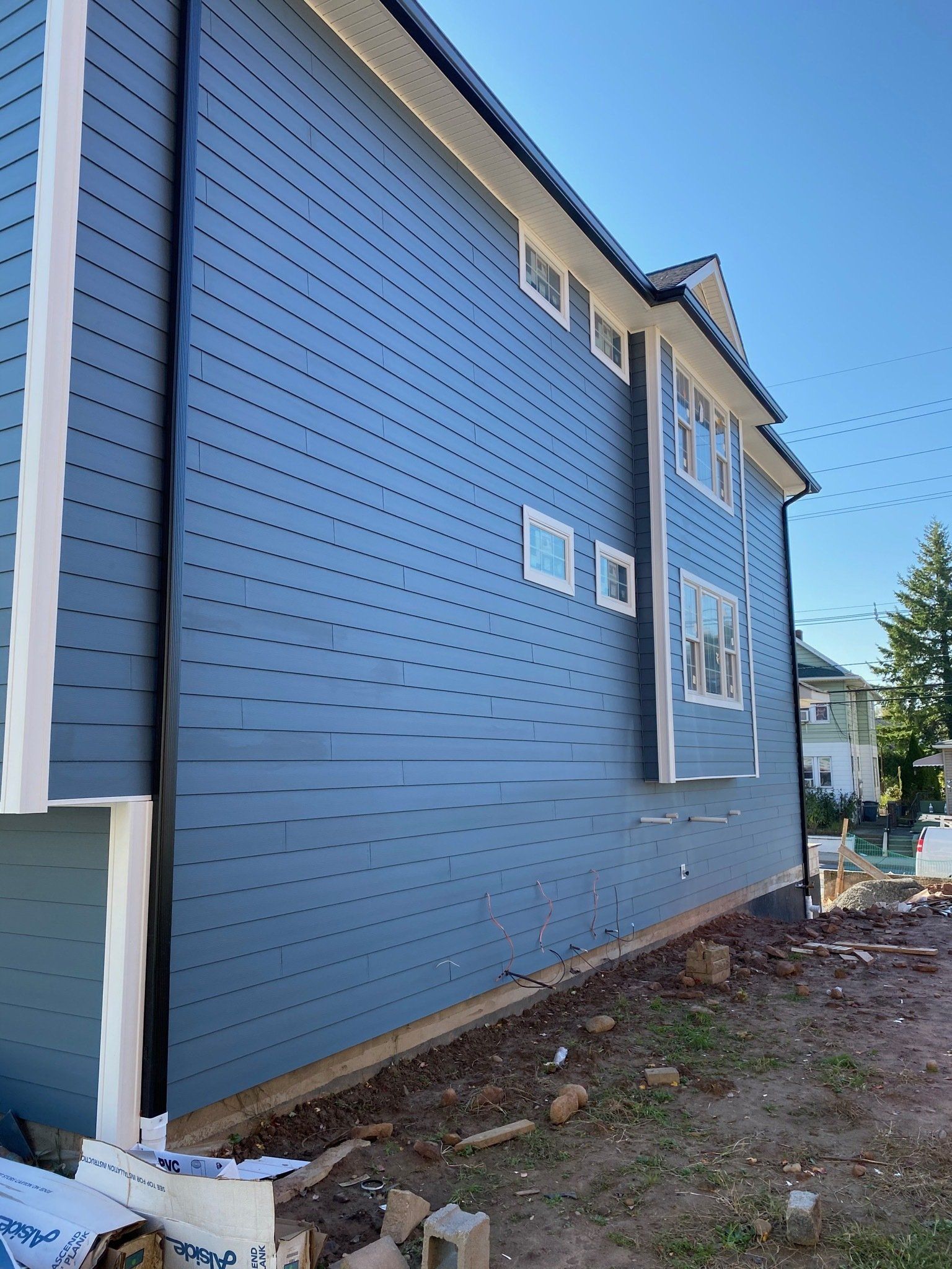 Blue house exterior with new siding, windows, and unfinished dirt yard along the side wall