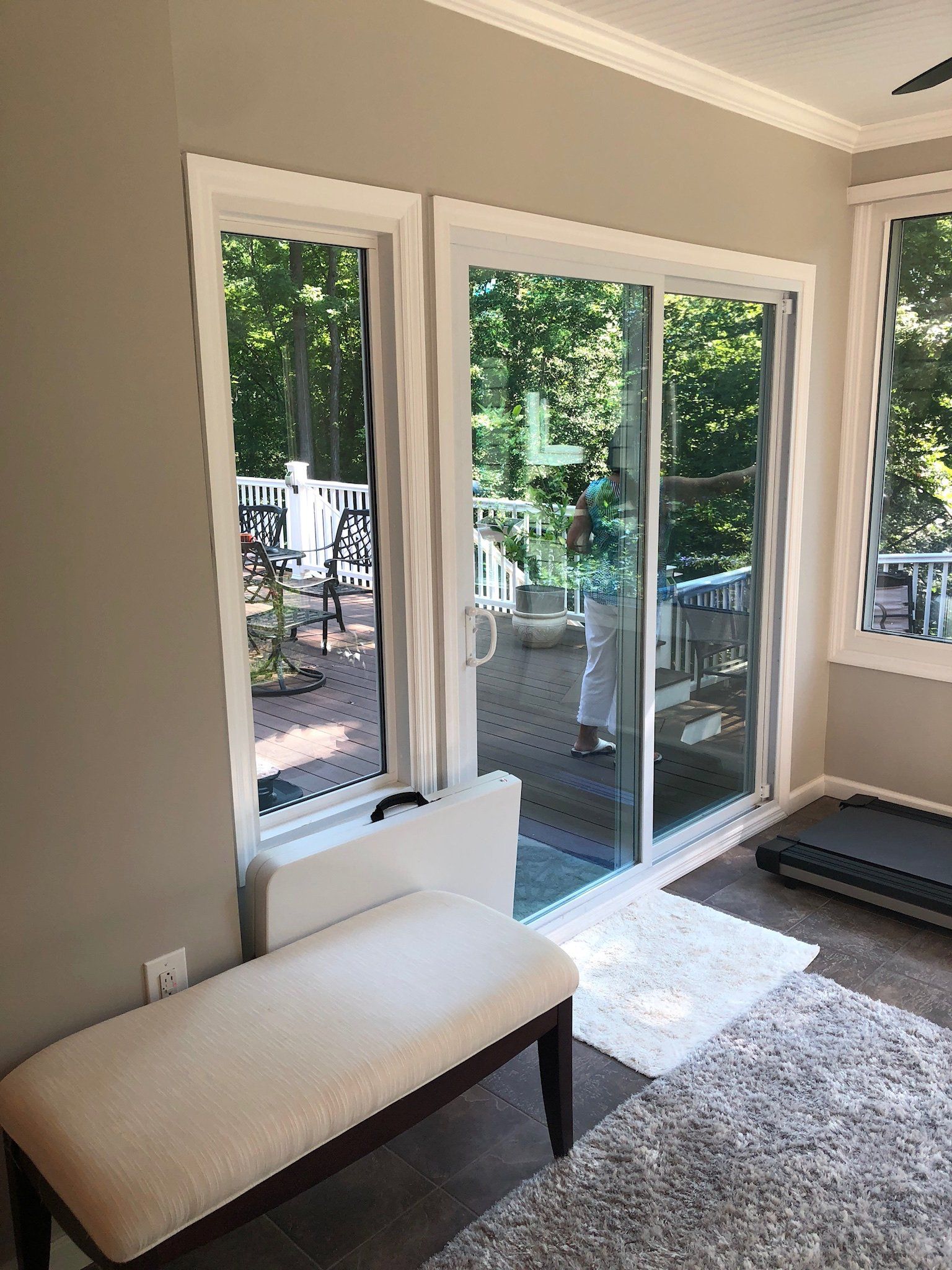 Sunlit room with sliding glass doors opening to a leafy patio, beige bench in foreground