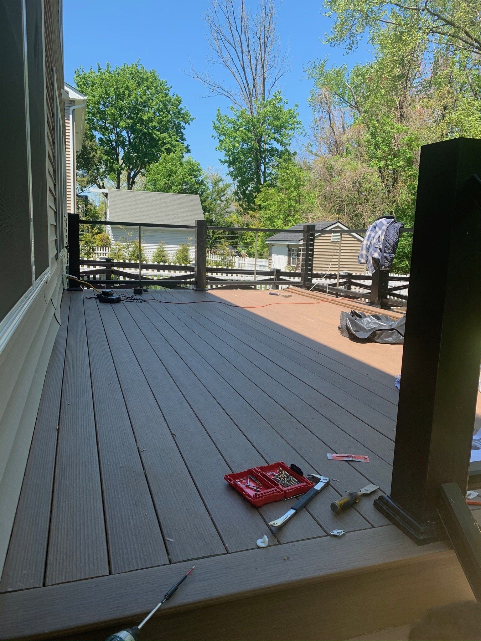Wooden deck with tools and a red toolbox in the foreground, trees and a person near the railing in the background