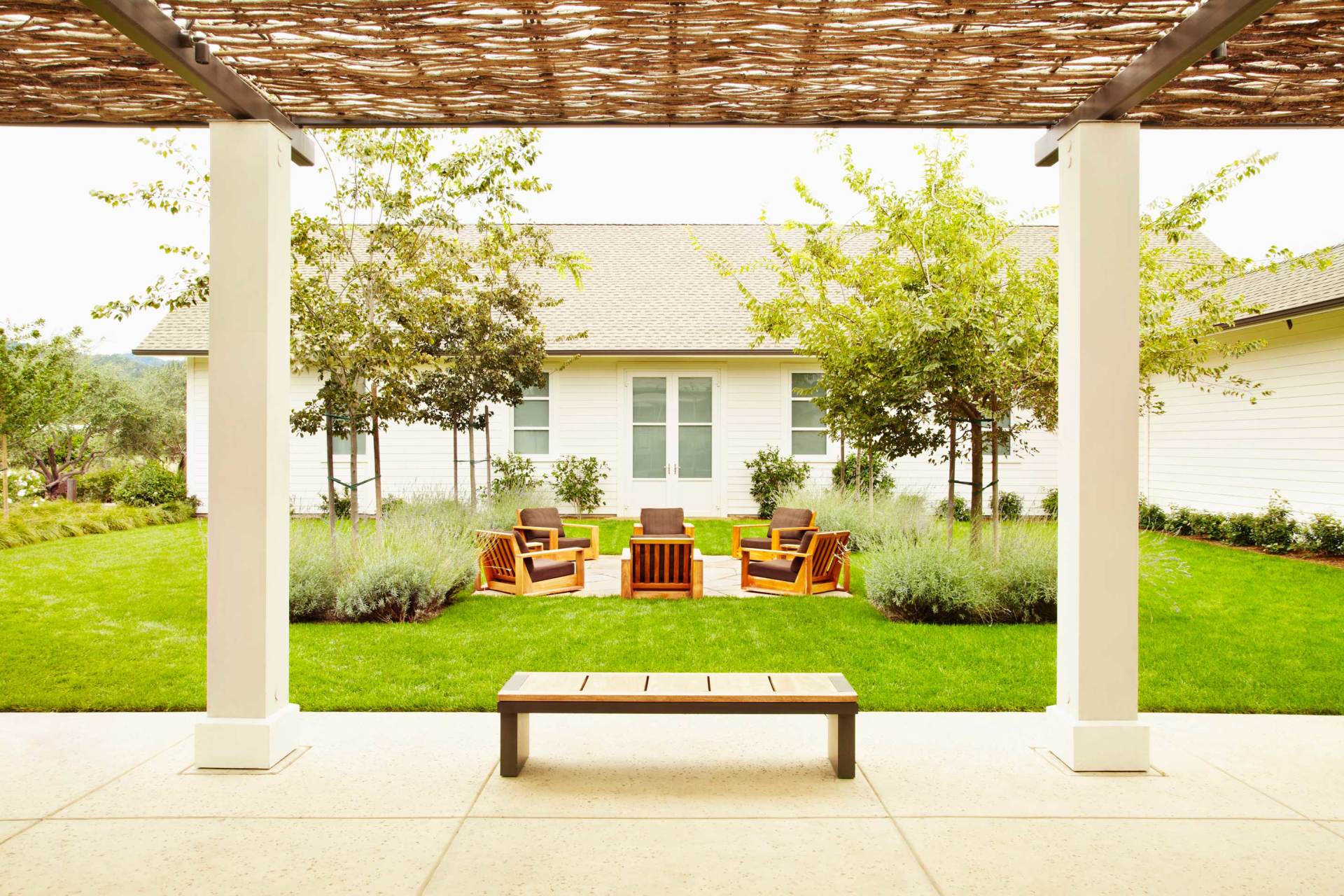 Modern patio with bench, white columns, and outdoor seating on a green lawn under a trellis