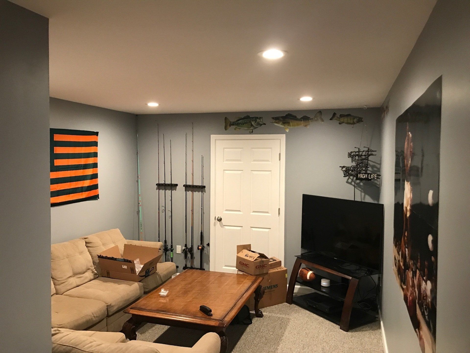 Small living room with beige sectional, coffee table, TV, gray walls, and orange-black wall art