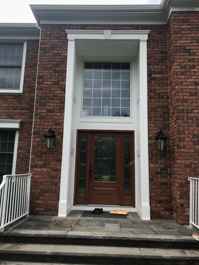 Brick townhouse entrance with white columns, steps, and a glass-paneled front door
