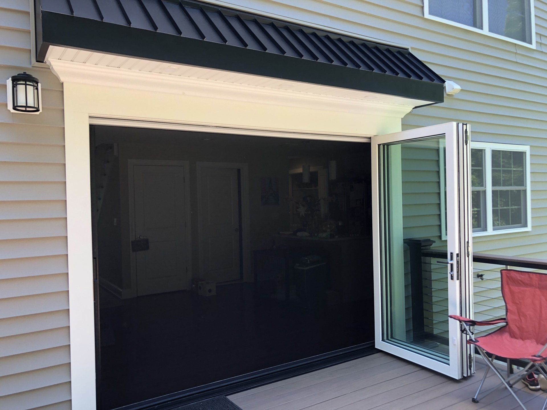 Open patio door leading into a dark garage with tan siding and a red chair outside