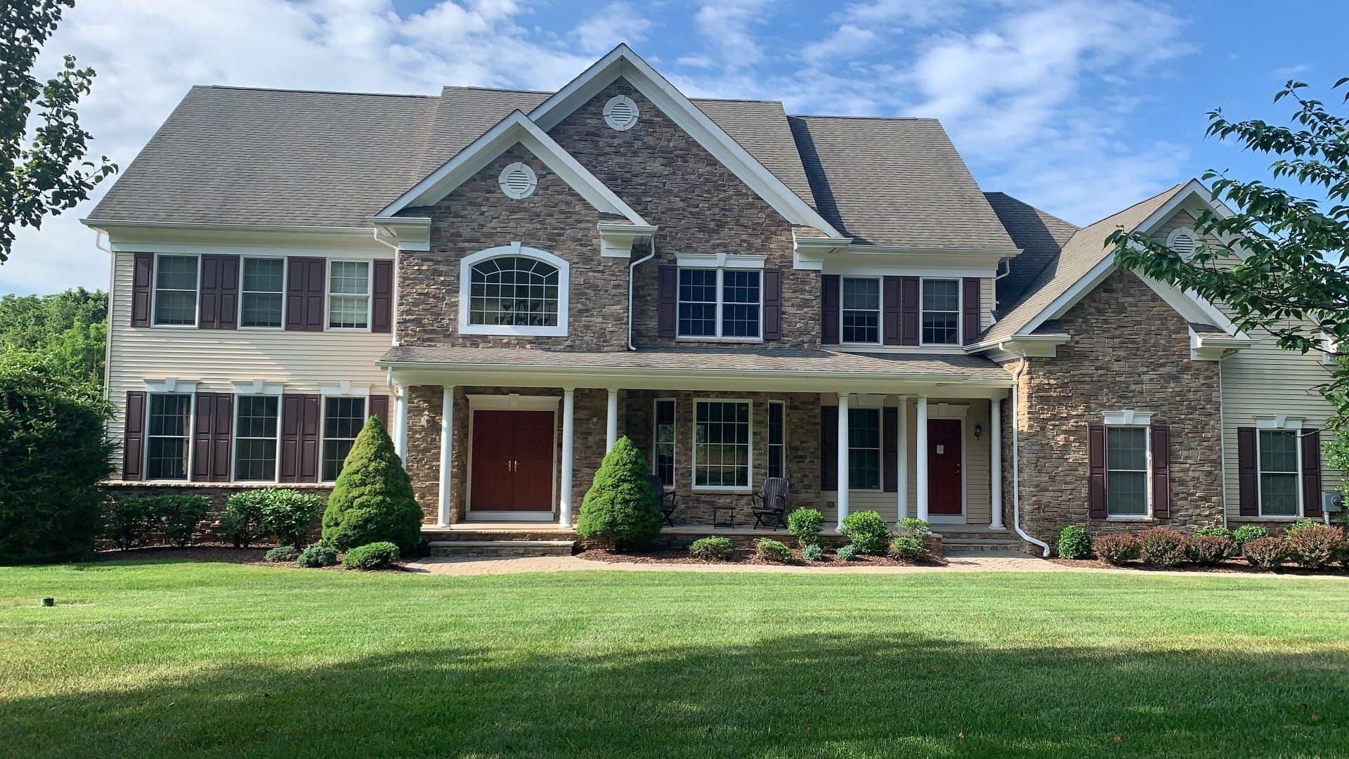 Large two-story suburban house with stone accents, a covered porch, and a manicured front lawn