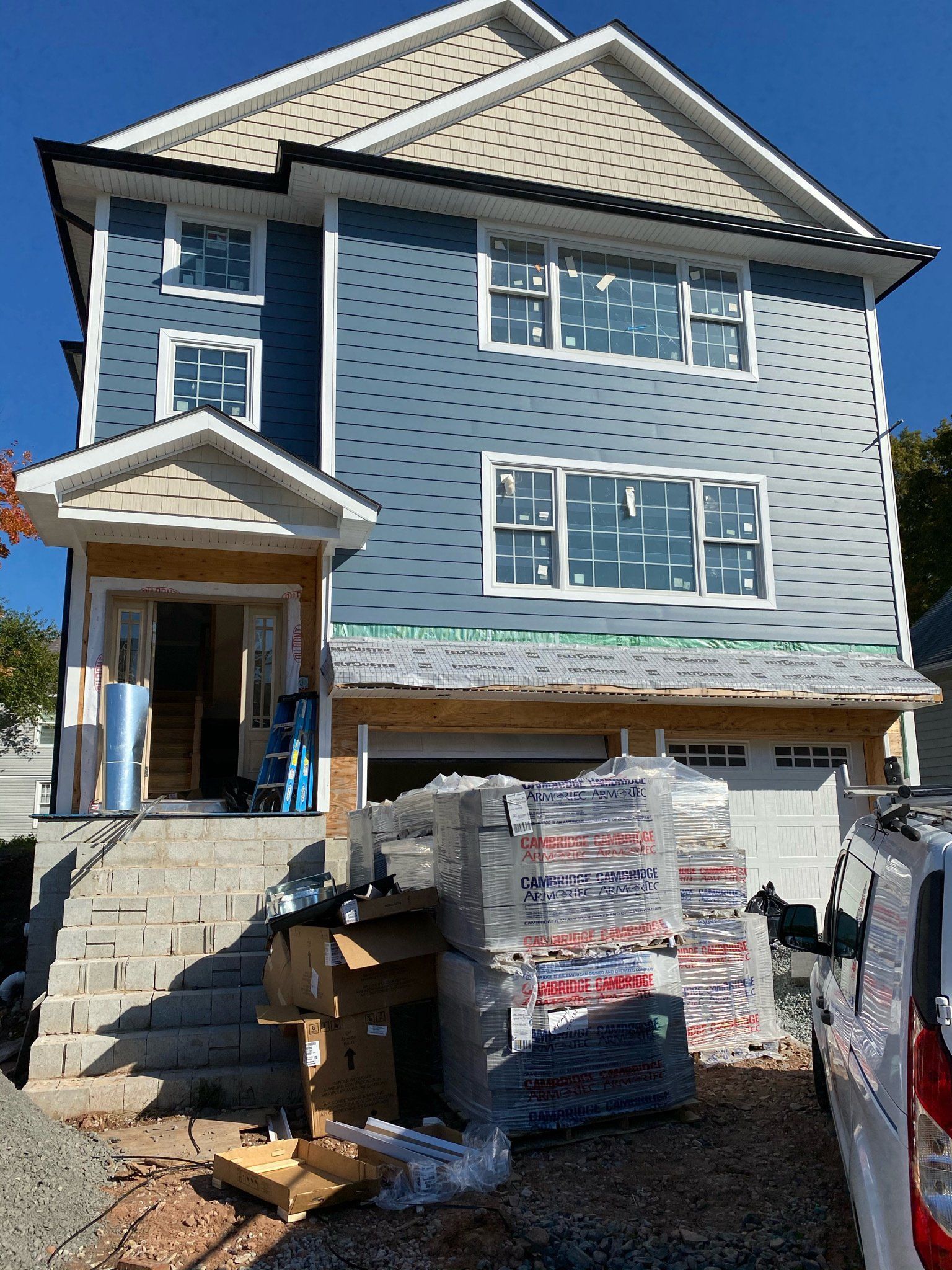 Newly built blue-gray house with construction materials stacked in front and a front porch under construction
