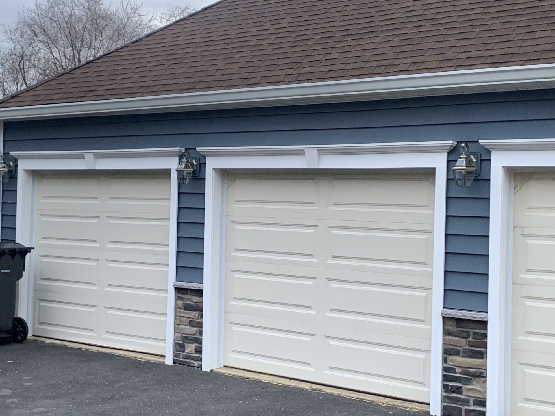 Three white garage doors on a blue house with white trim and stone accents