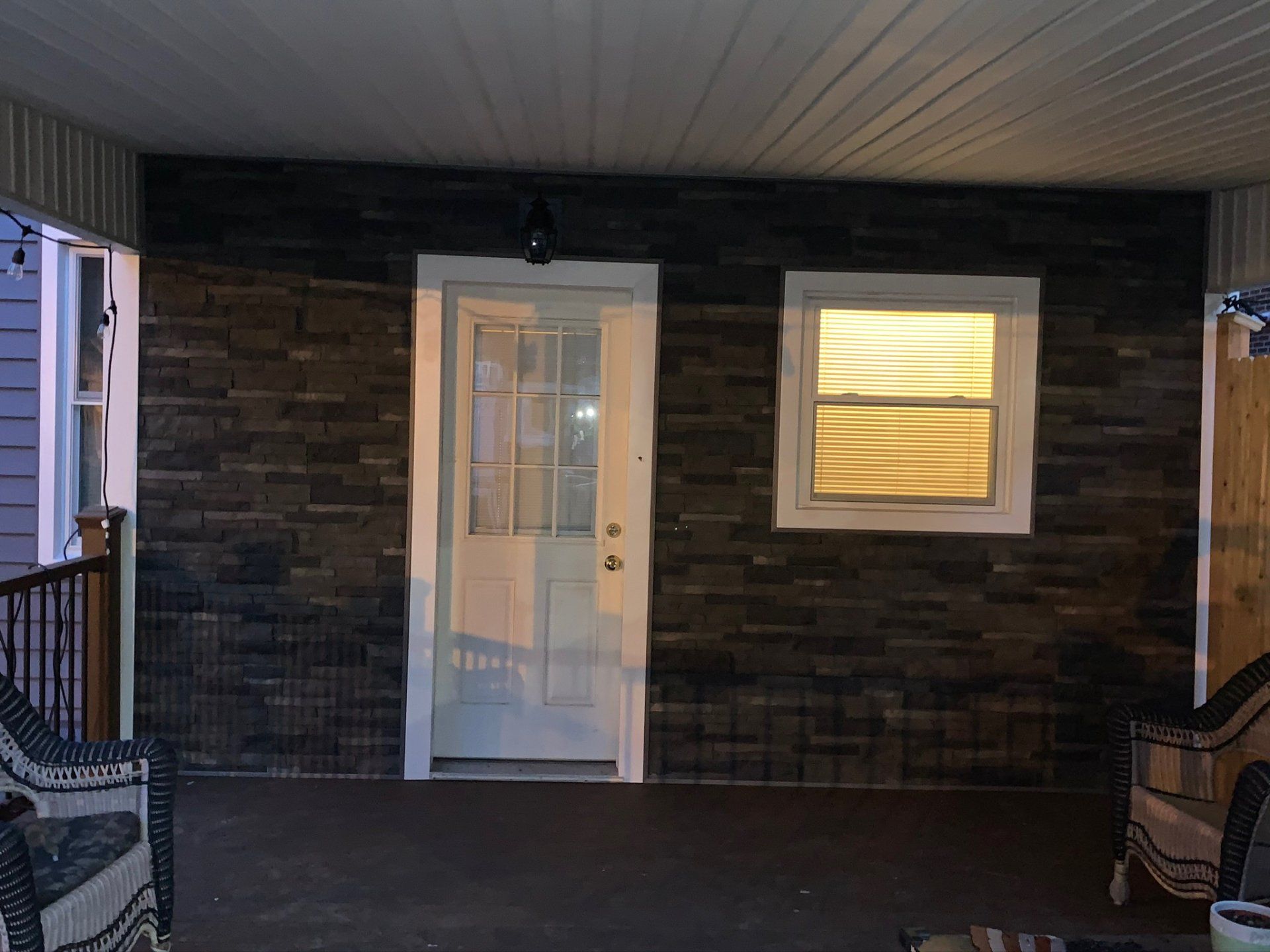 Covered porch with a white door, lit window, and chairs on either side.