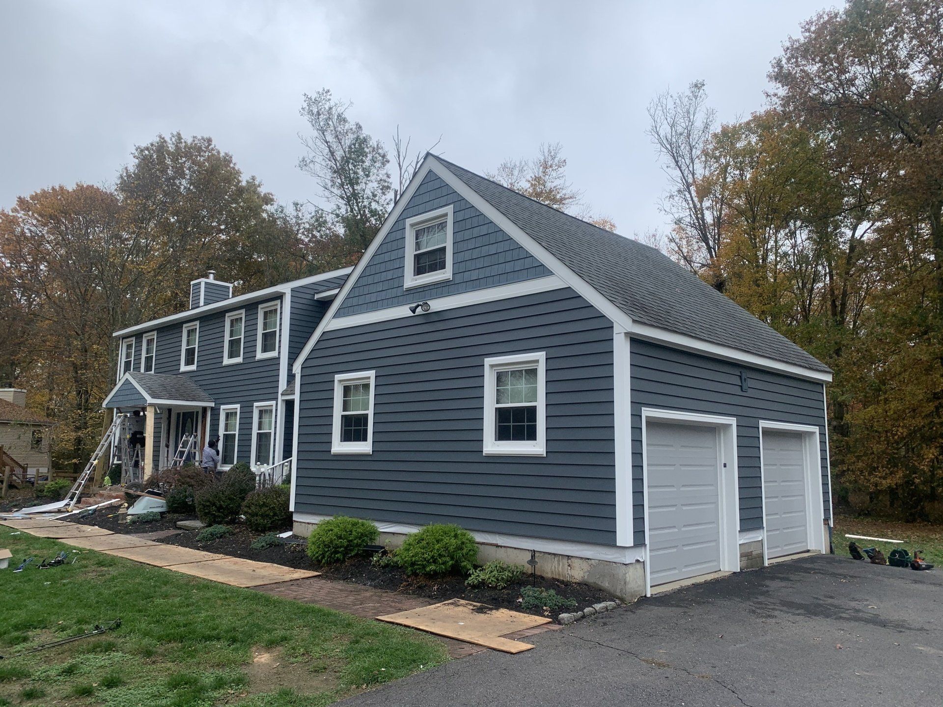 Gray two-story house with white trim, attached garage, and autumn trees in the background