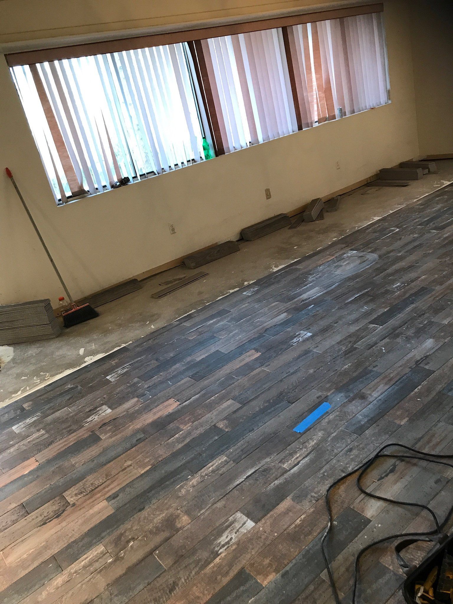 Empty room with unfinished wood floor, windows with blinds, and a coiled cable on the floor