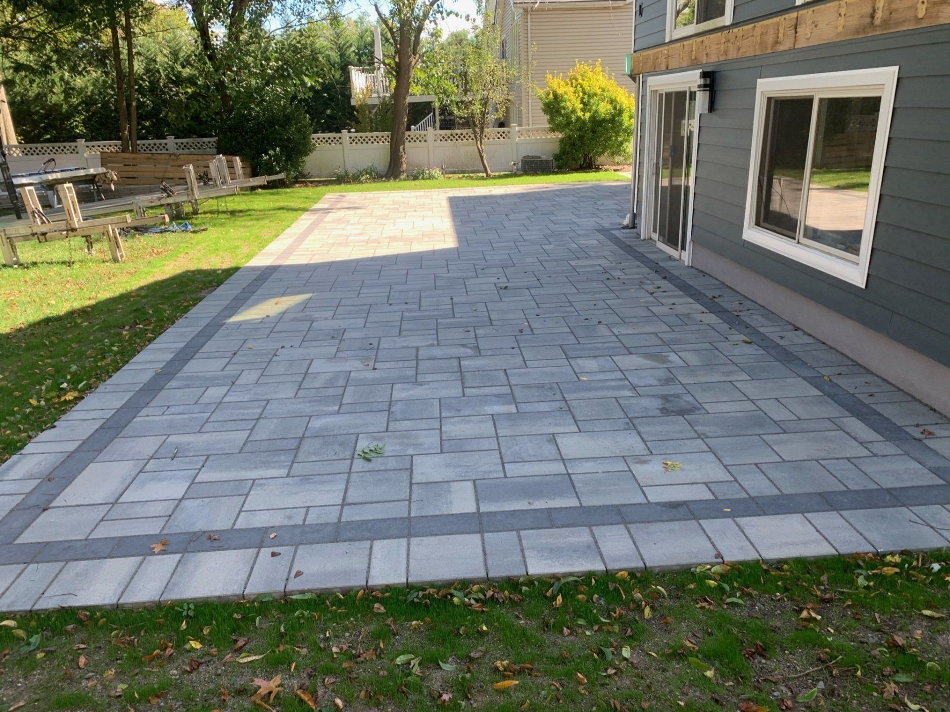 Backyard patio with gray paver stones beside a house and lawn
