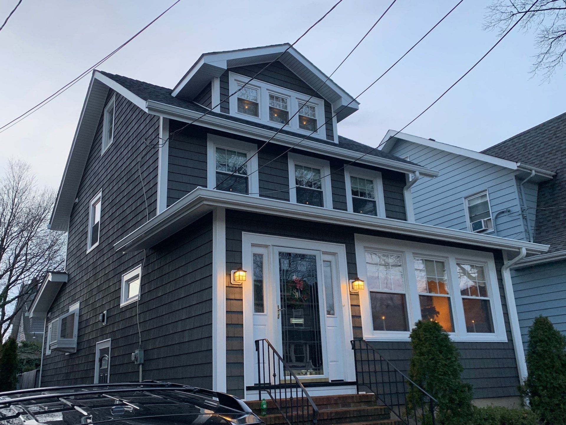 Gray three-story house with white trim and lit porch lights at dusk