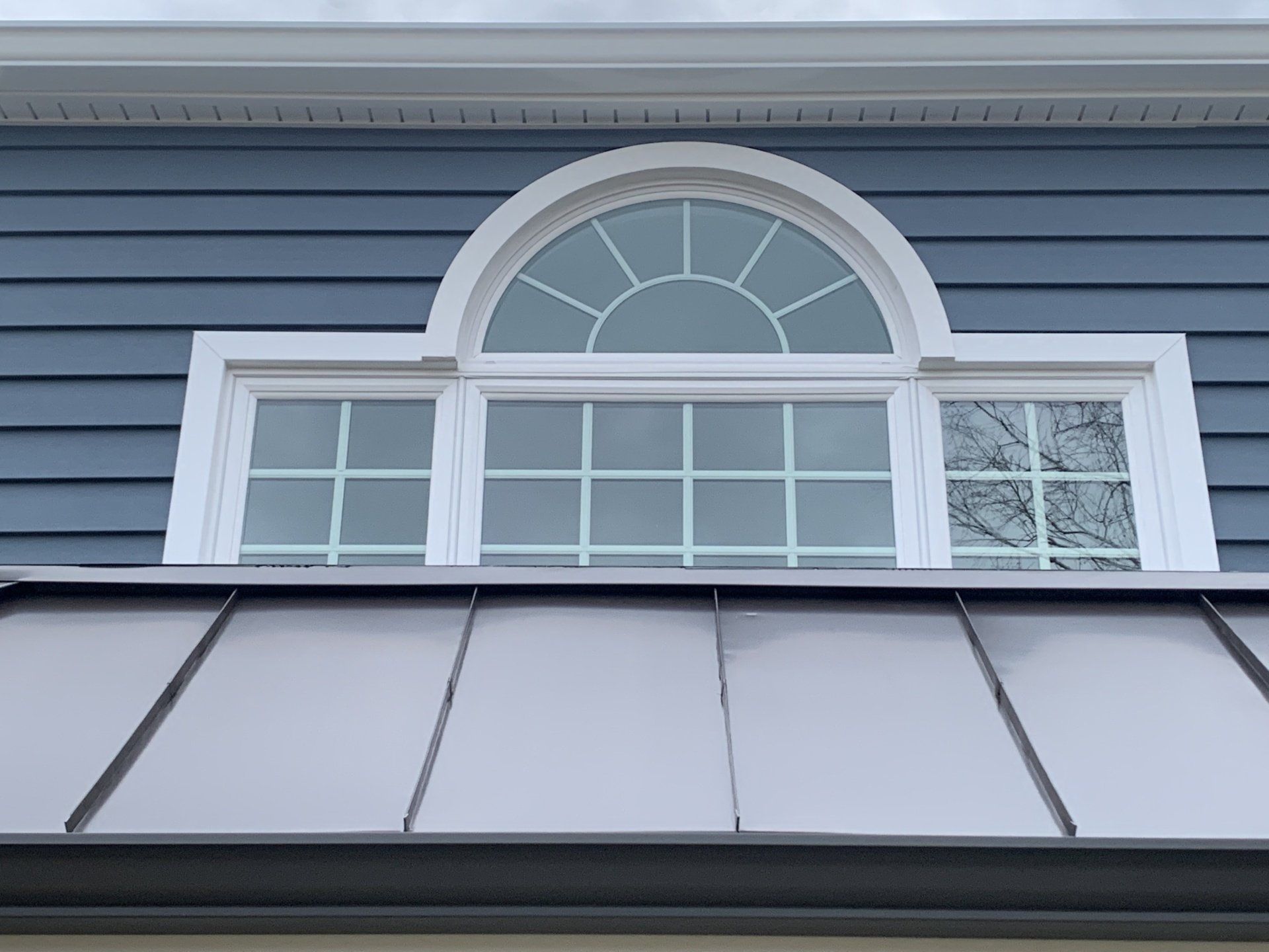 Blue house exterior with a white arched window and gray metal roof