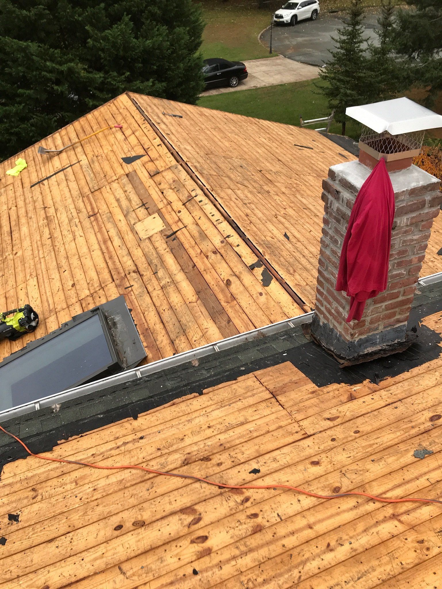 Roof under construction with exposed wood sheathing, a brick chimney, and a red tarp draped over it.