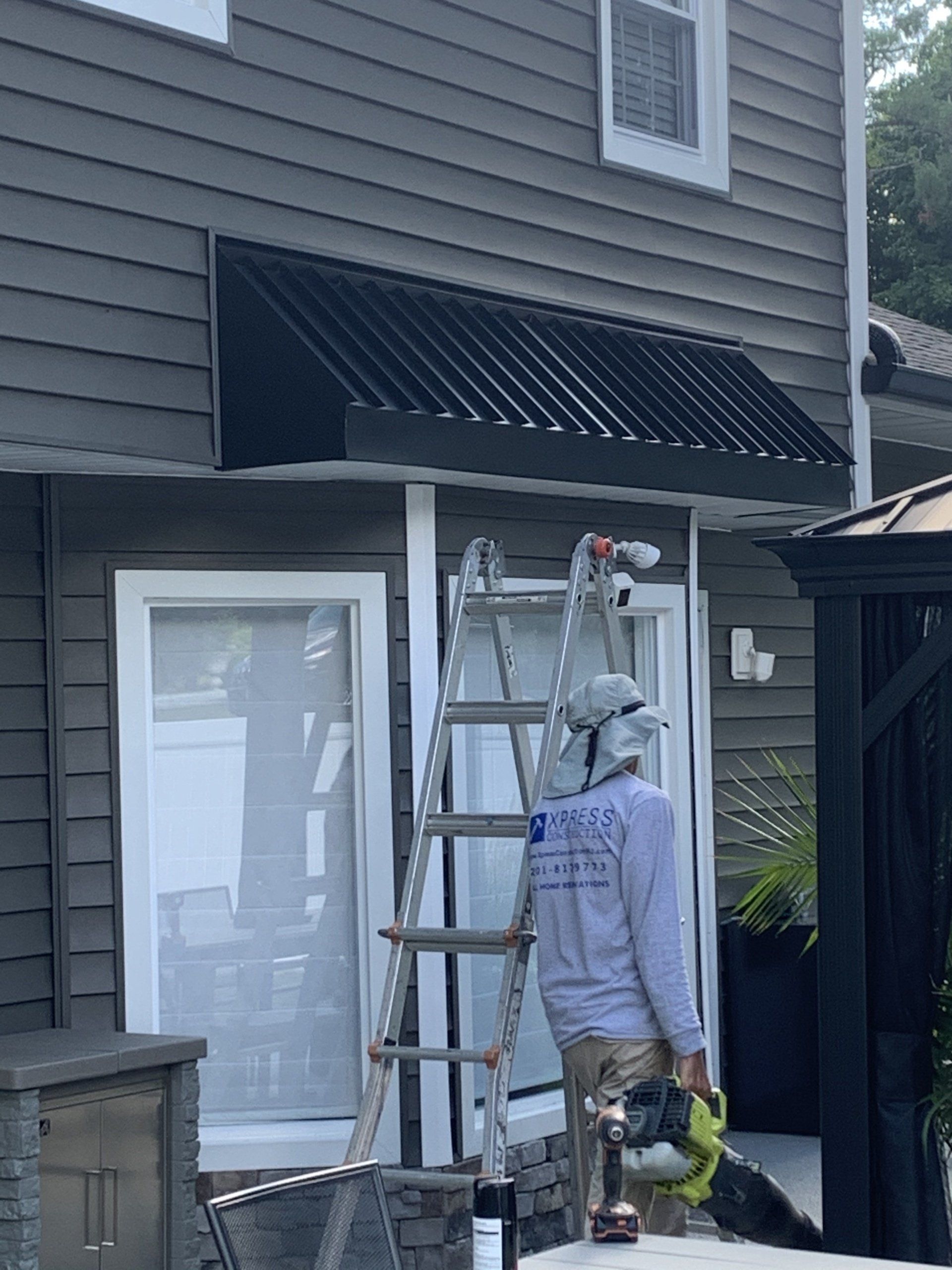 Person on a ladder painting an awning above a sliding glass door on a house