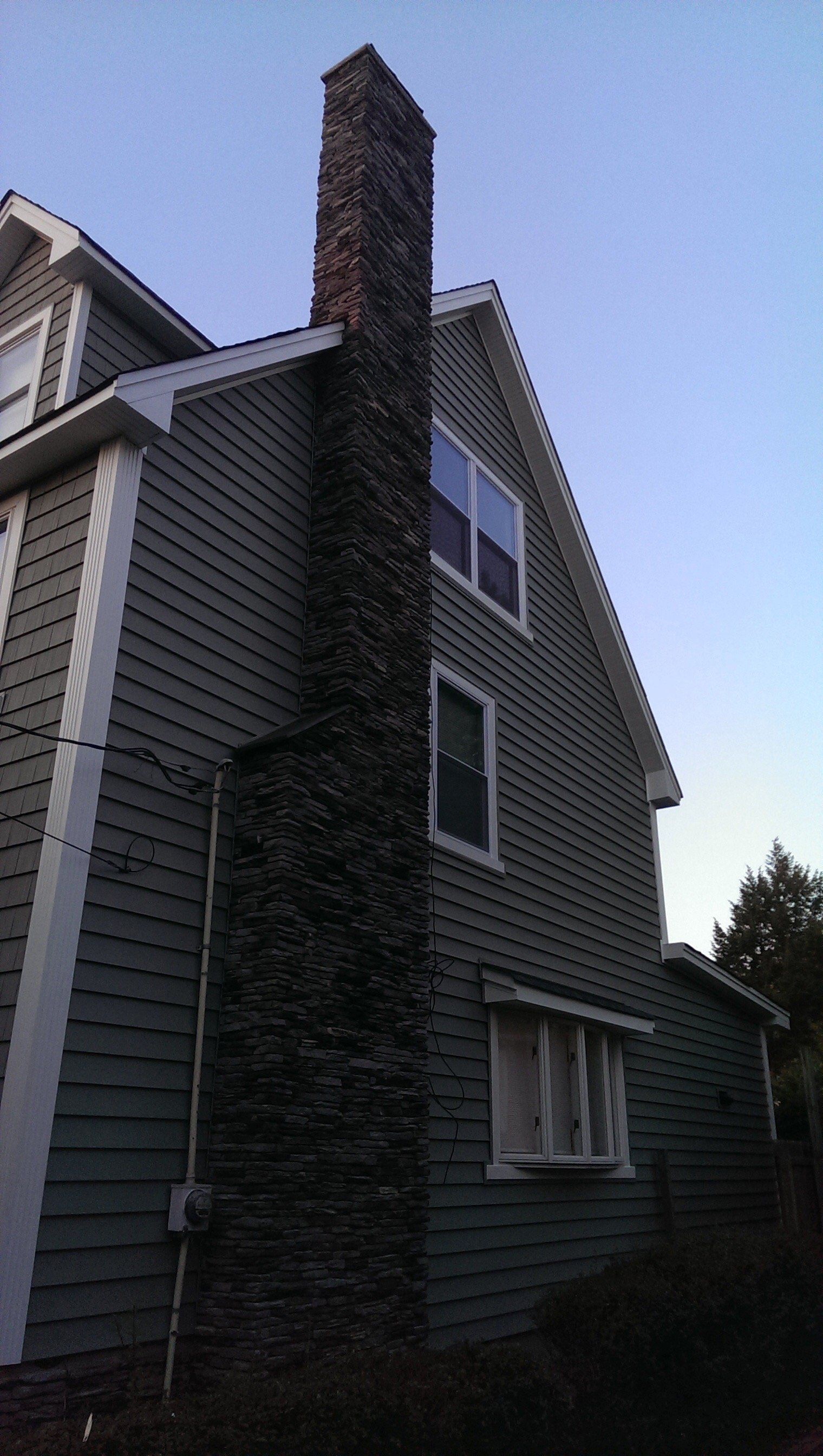 Side view of a gray house with a tall brick chimney and dark roof at dusk