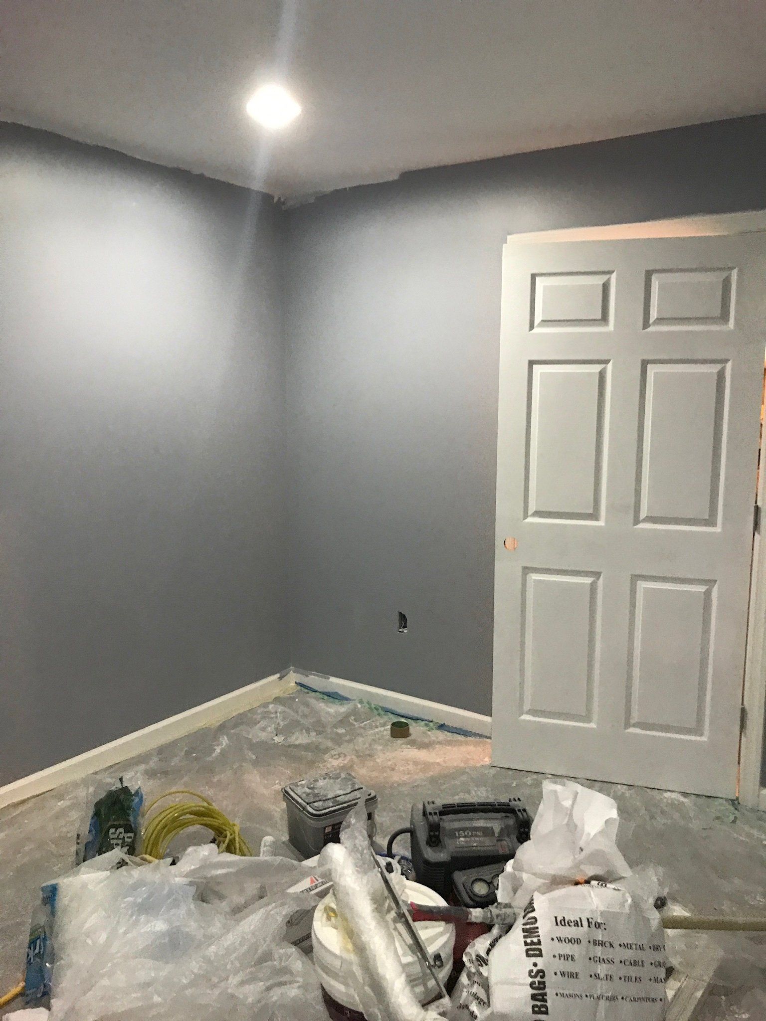 Empty gray room under renovation with a white door and tools on the floor