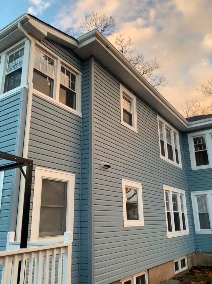 Blue two-story house exterior with white trim and windows at sunset