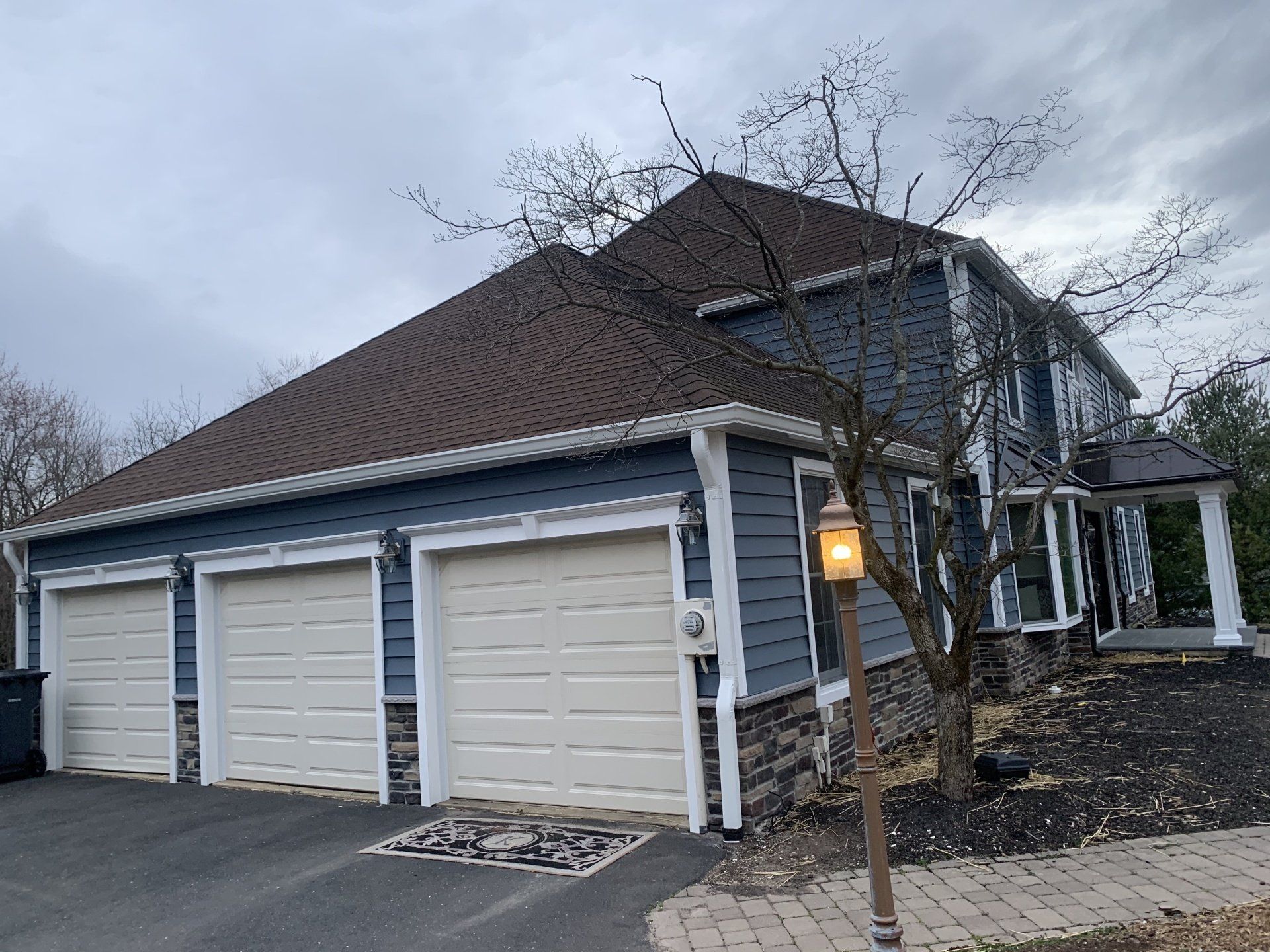 Suburban house with three-car garage, white siding, brown roof, and a lit lamp post at dusk