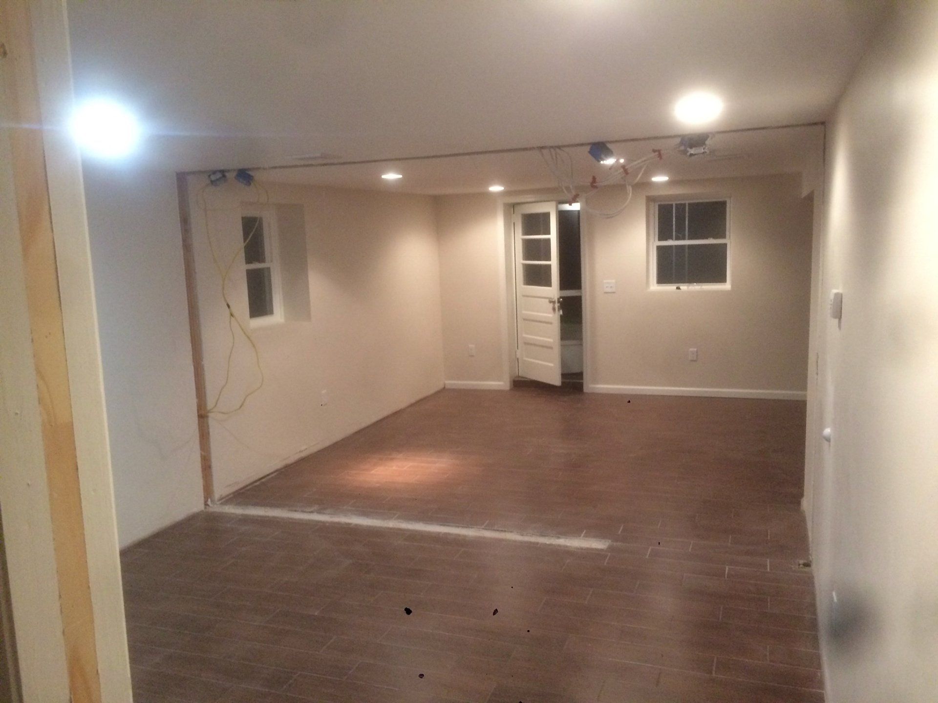 Empty beige room with wood floors, recessed lights, and windows at the far end