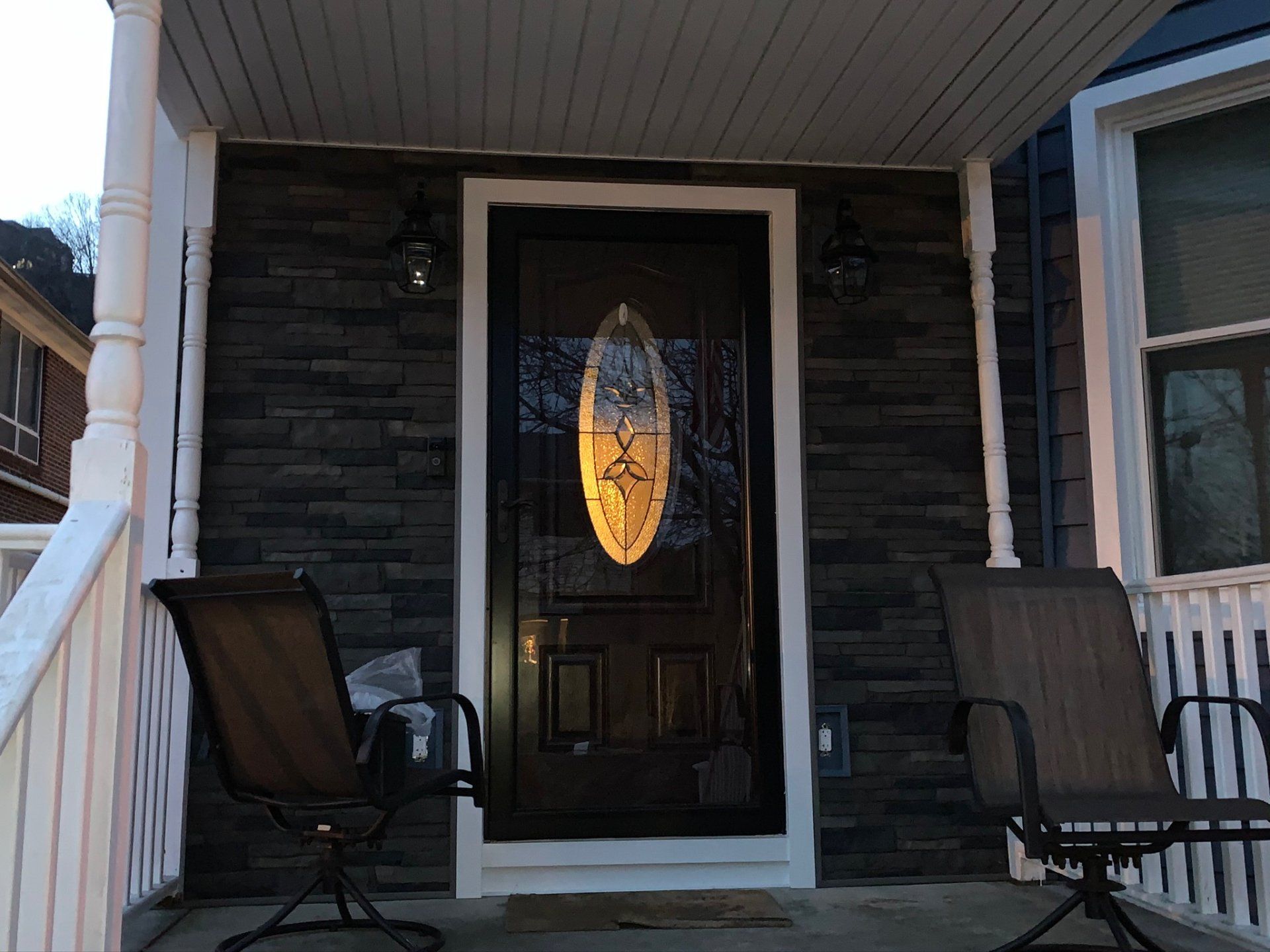 Front porch with a black front door, stone facade, and two patio chairs.