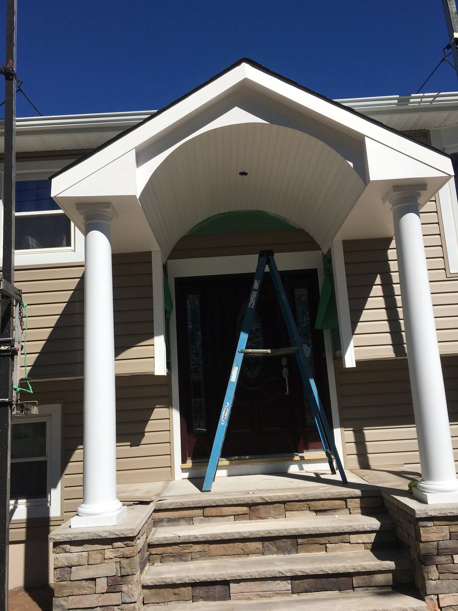 Front porch with white columns, arched entry, and a ladder on the steps of a beige house