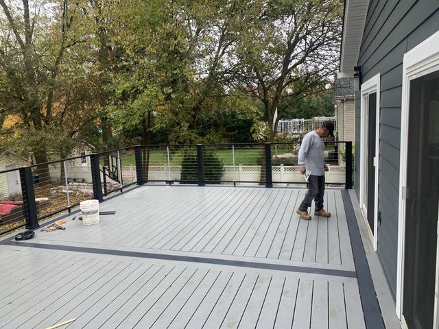 Gray deck with black railing beside a house, with a person standing near the sliding doors.
