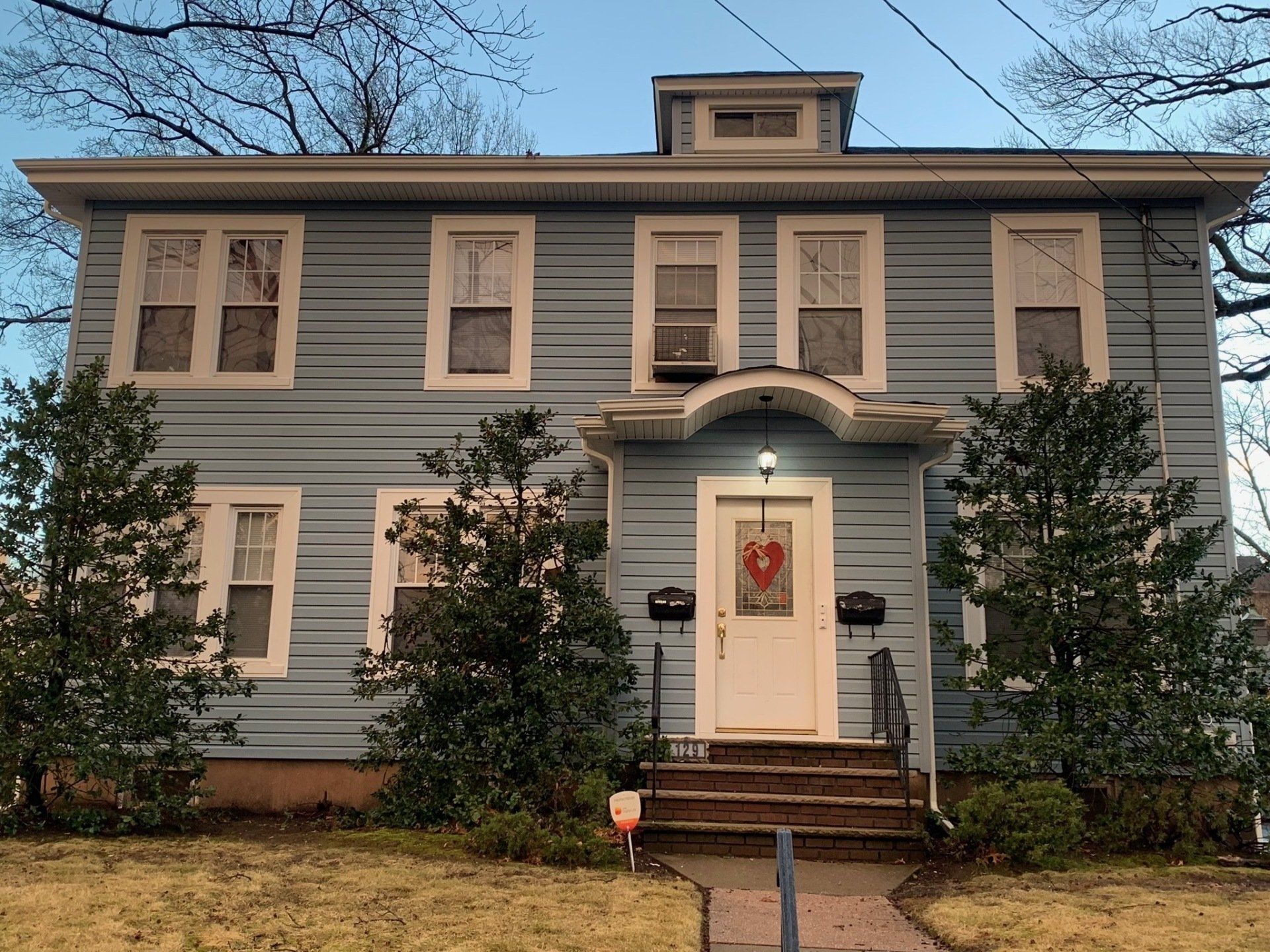 Gray two-story house with white trim, front porch, and red wreath on the front door