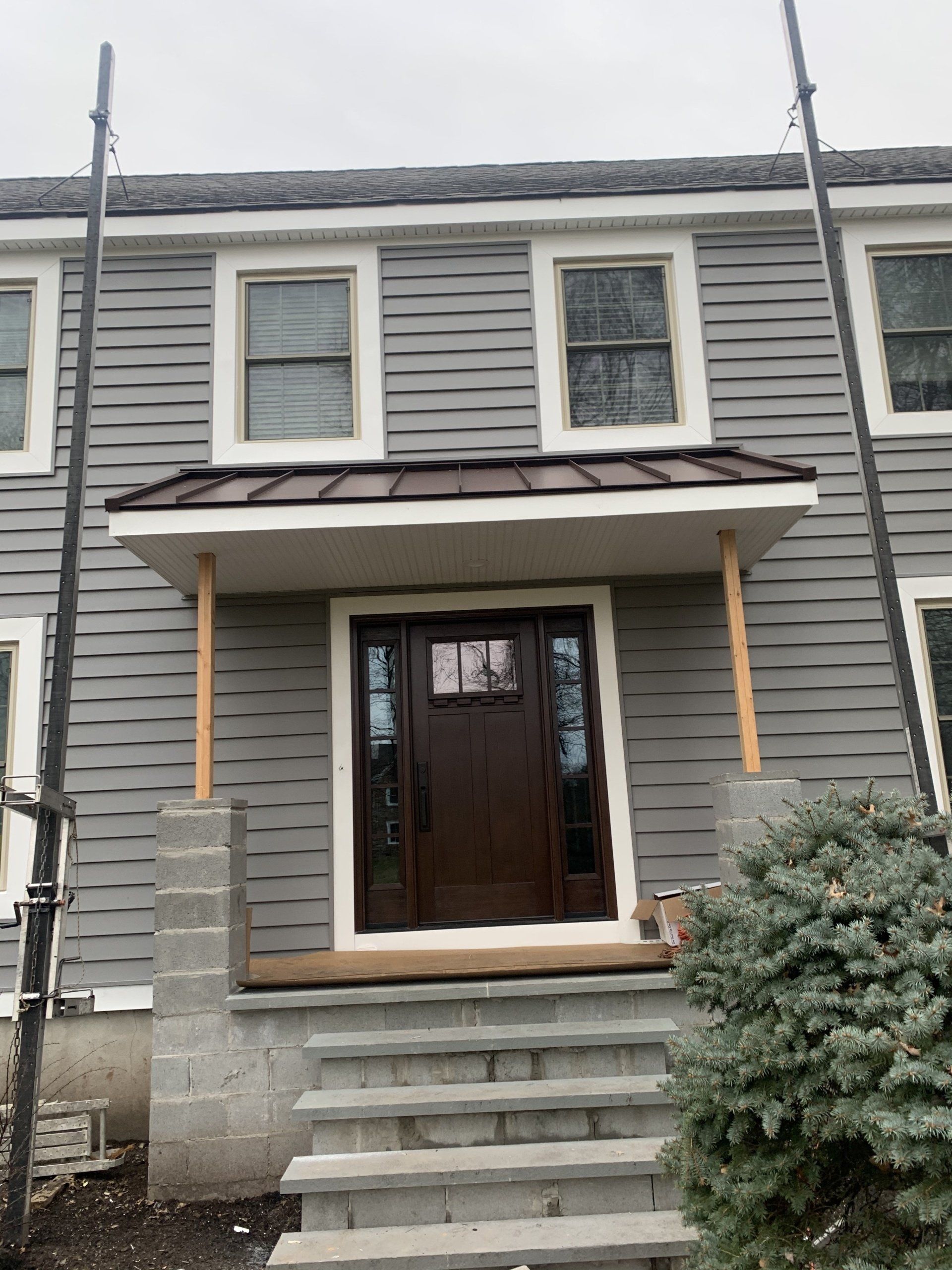 Gray house front entrance with steps, small porch, and dark wood door under a brown awning